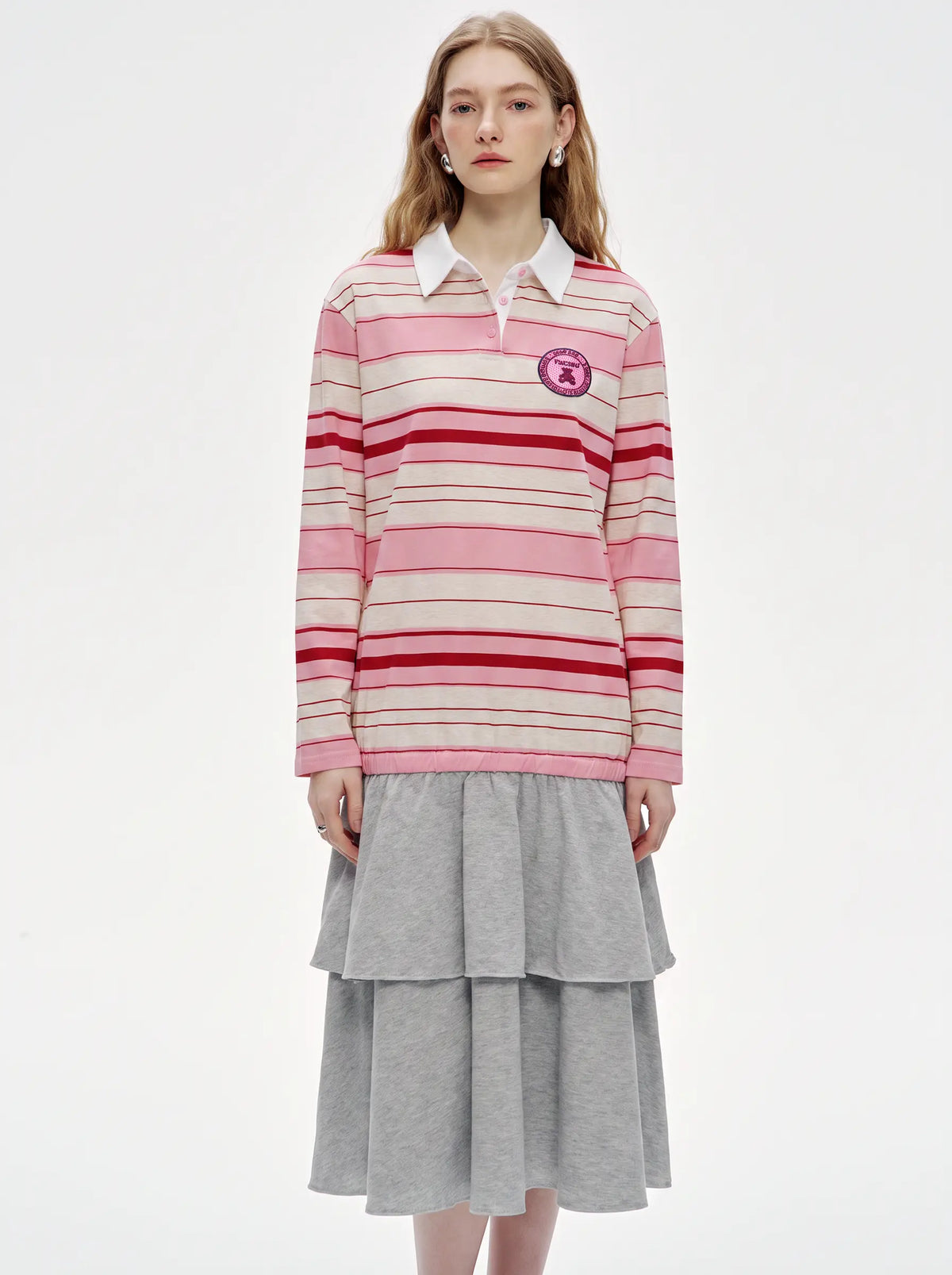 A model wearing a pink and red striped long-sleeve rugby shirt with a white collar, layered over a gray tiered skirt, against a plain white studio background. TCH Women's Striped Polo Mini Dress