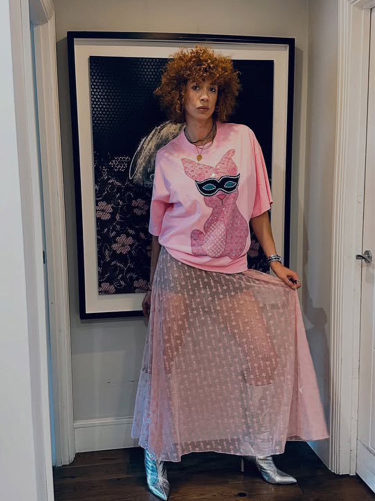 Person wearing a pink outfit with a graphic design in a room with a framed picture on the wall.