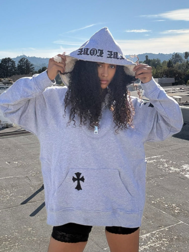 A person wearing a white hoodie with a cross patch on the hood and text on the sleeves, standing on a rooftop.