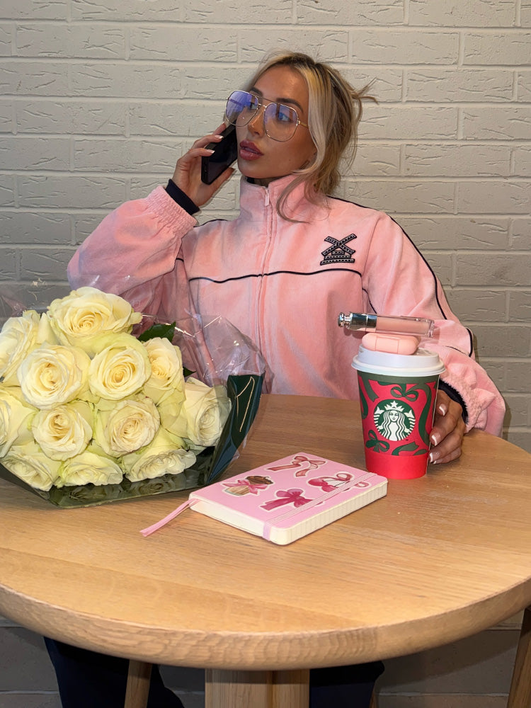 Person in pink jacket with Starbucks cup and flowers on a table against a brick wall.