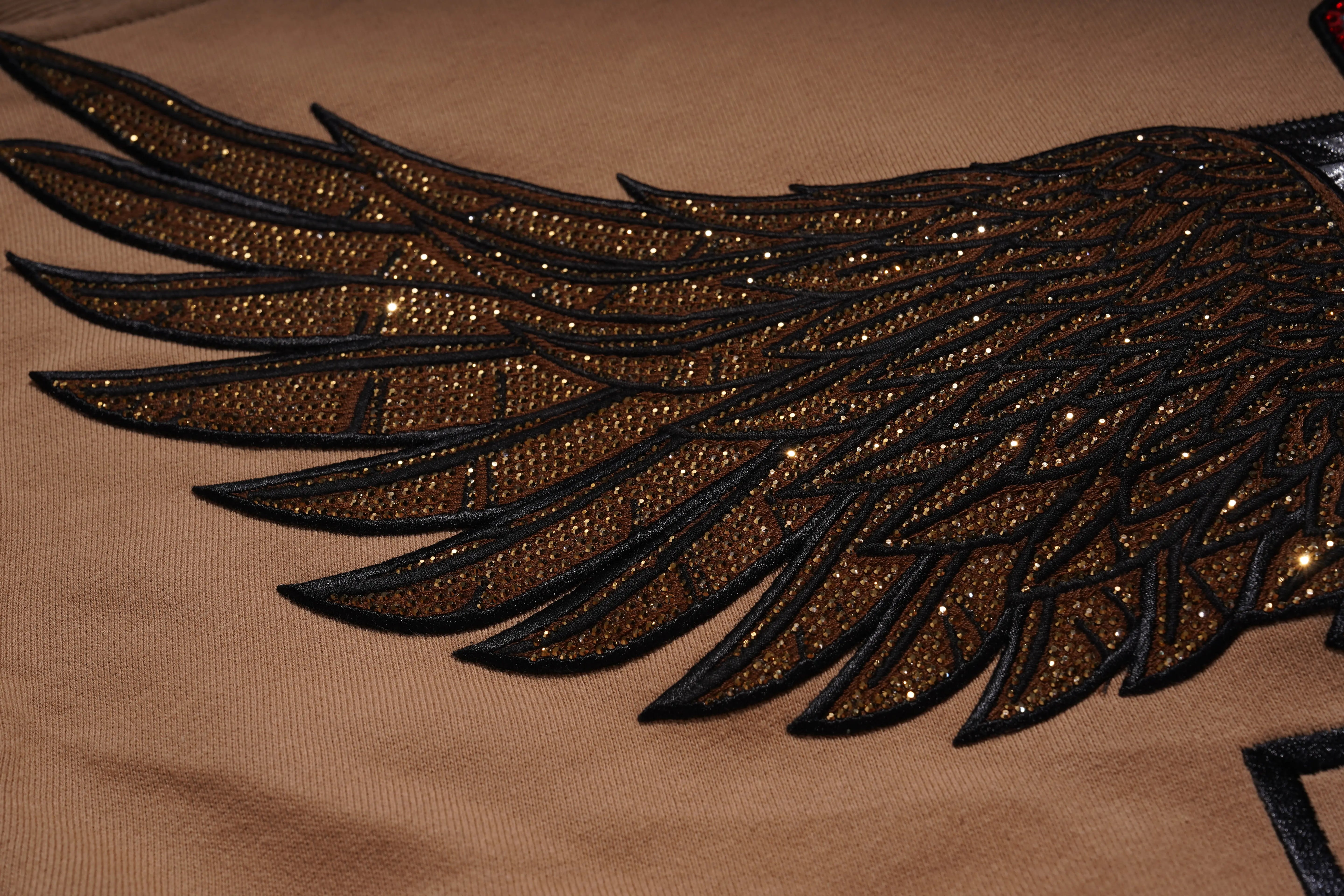 Decorative black and gold winged design on a beige background， Rhinestone Wing Logo Sweatshirt