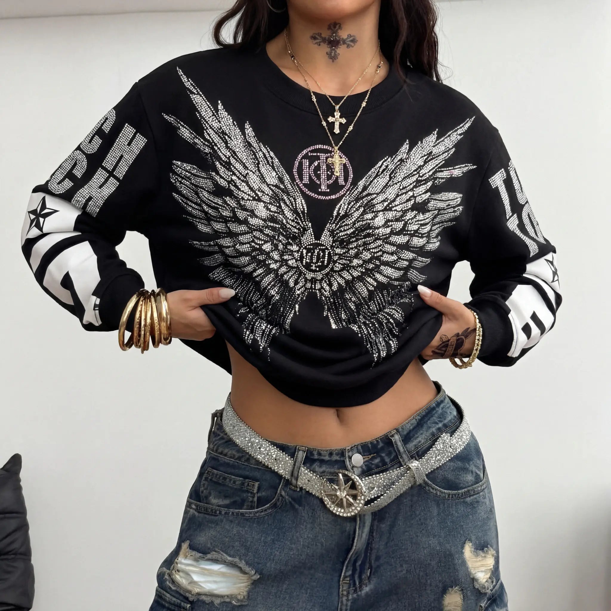 Person wearing a black sweater with a large white wing design and ripped jeans. TCH 1976 Rhinestone Wings Sweatshirt