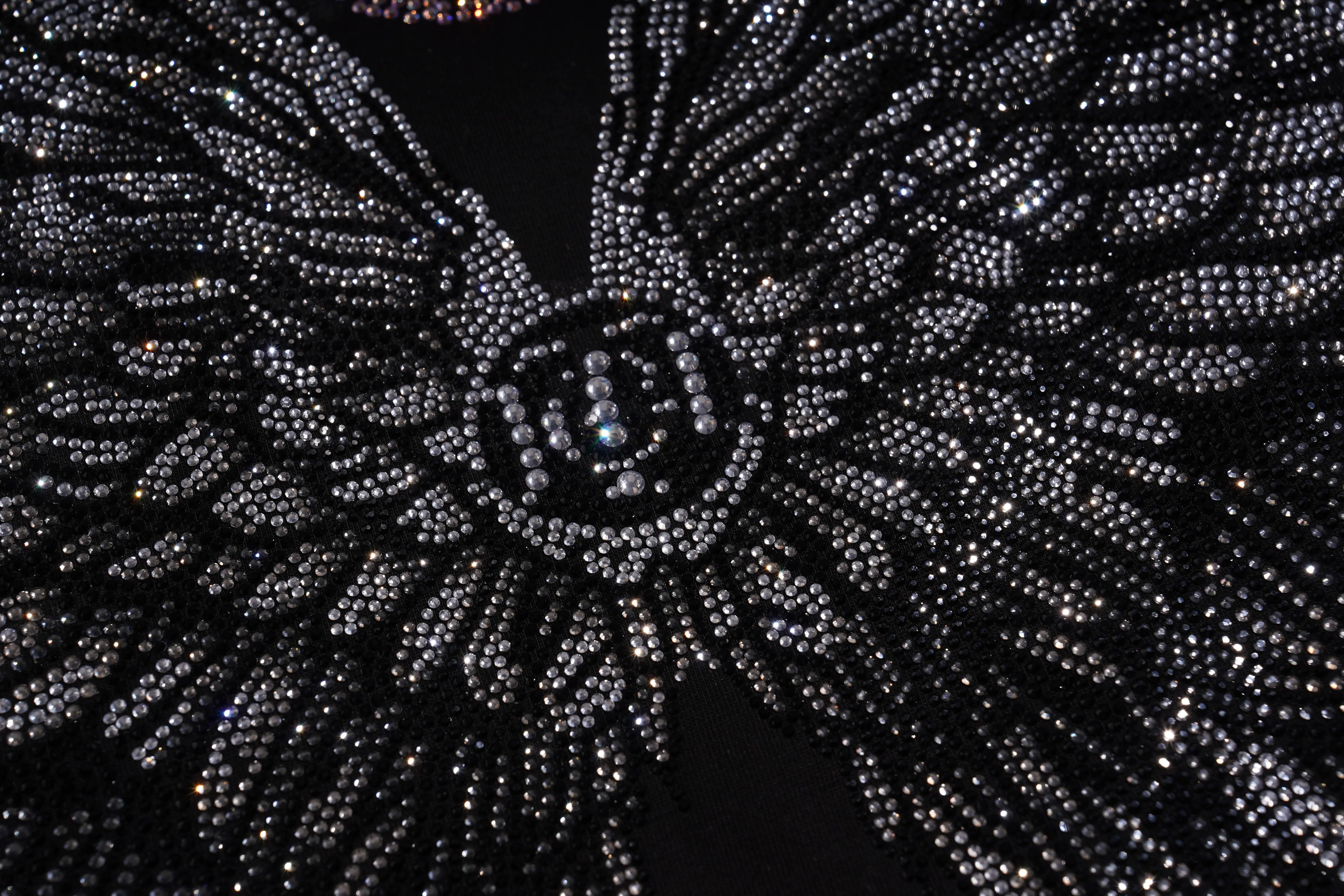 Close-up of a black and silver beaded fabric with a starburst pattern. TCH 1976 Rhinestone Wings Sweatshirt