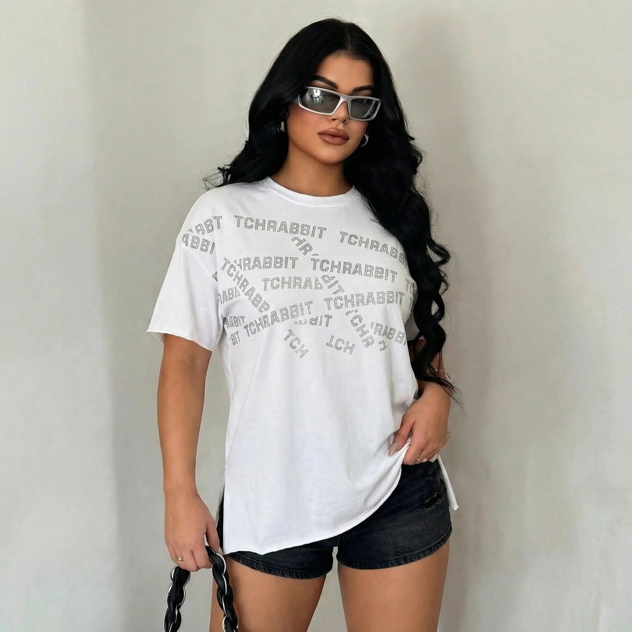 Woman wearing a white t-shirt with text and black shorts against a plain background, TCH All-Over TCHRABBIT Logo T-Shirt