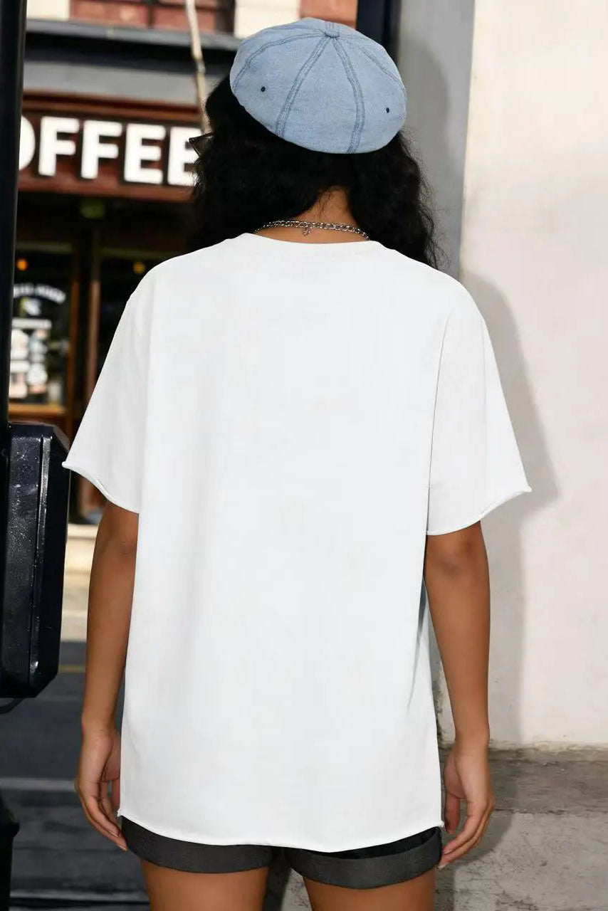 Person wearing a white t-shirt and black shorts with a blue cap, standing in front of a coffee shop. TCH All-Over TCHRABBIT Logo T-Shirt