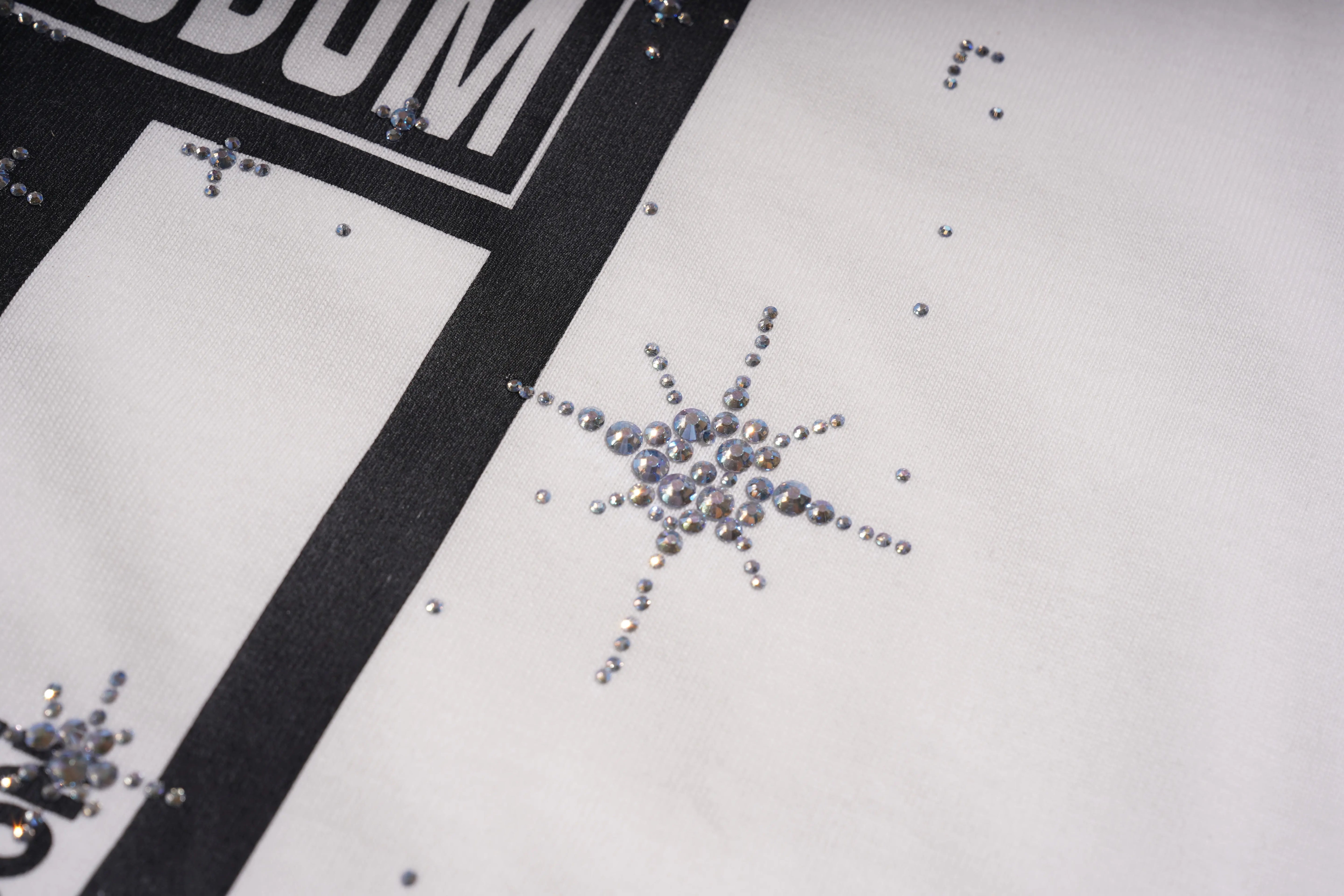 Close-up of decorative crystals on a white surface with a black border. TCH Anarchy Graphic Rhinestone T-Shirt