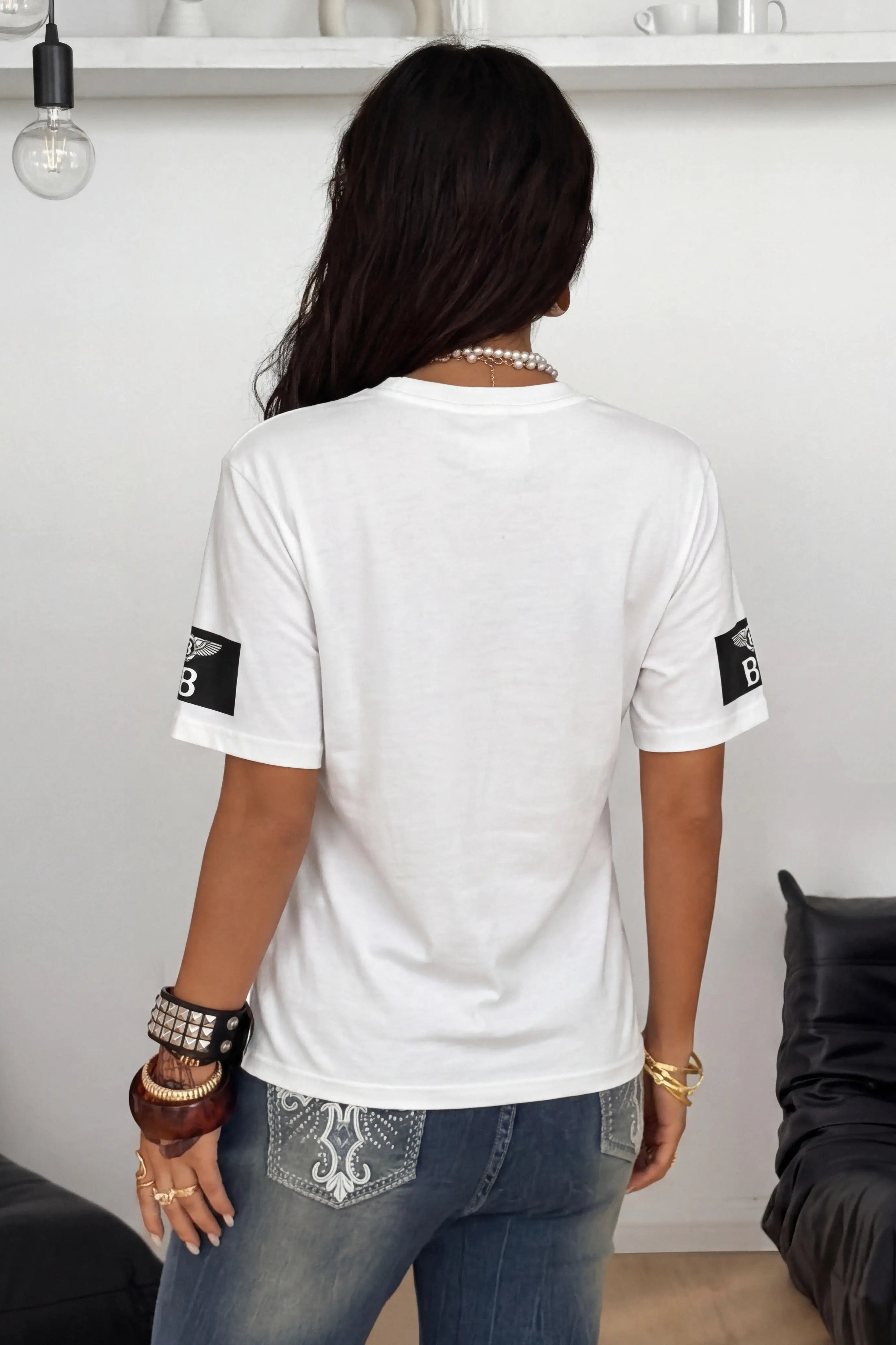 Person wearing a white t-shirt with black logos in a minimalistic room. TCH Anarchy Graphic Rhinestone T-Shirt
