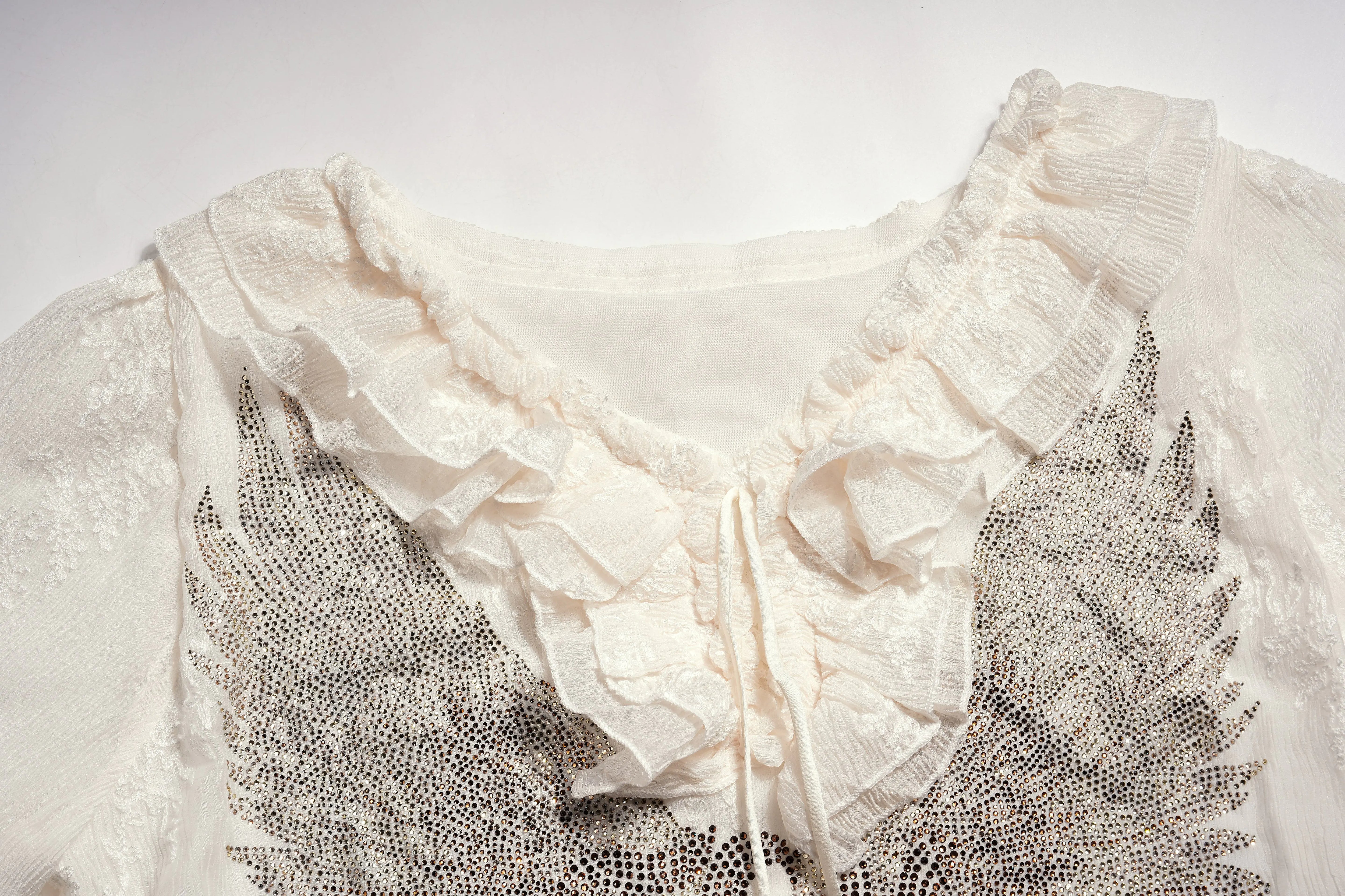 Close-up of a white lace garment with intricate detailing on a light background, TCH Angel Wings Rhinestone Ruffle Blouse