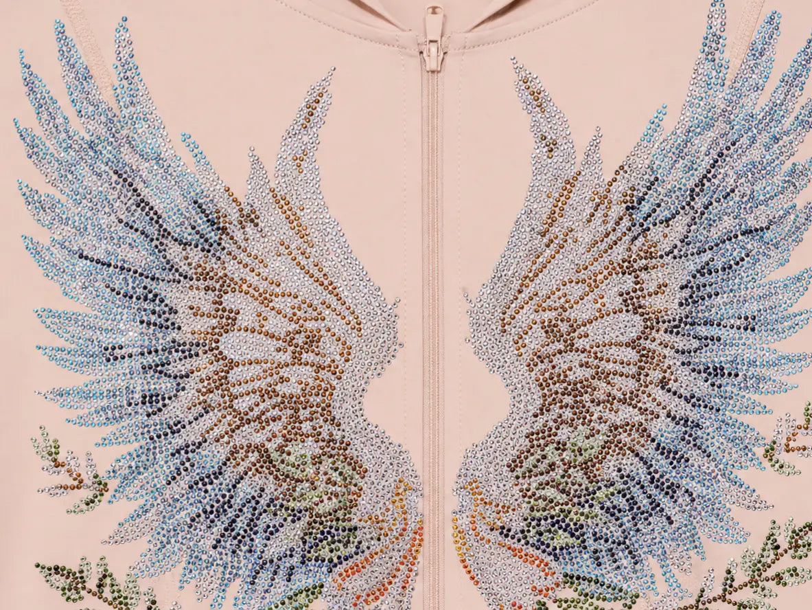 Close-up of a light pink zip-up hoodie featuring large, intricate beaded wing designs in shades of blue, brown, and green on both sides of the zipper. TCH Angel Wings Rhinestone Zip-Up Hoodie