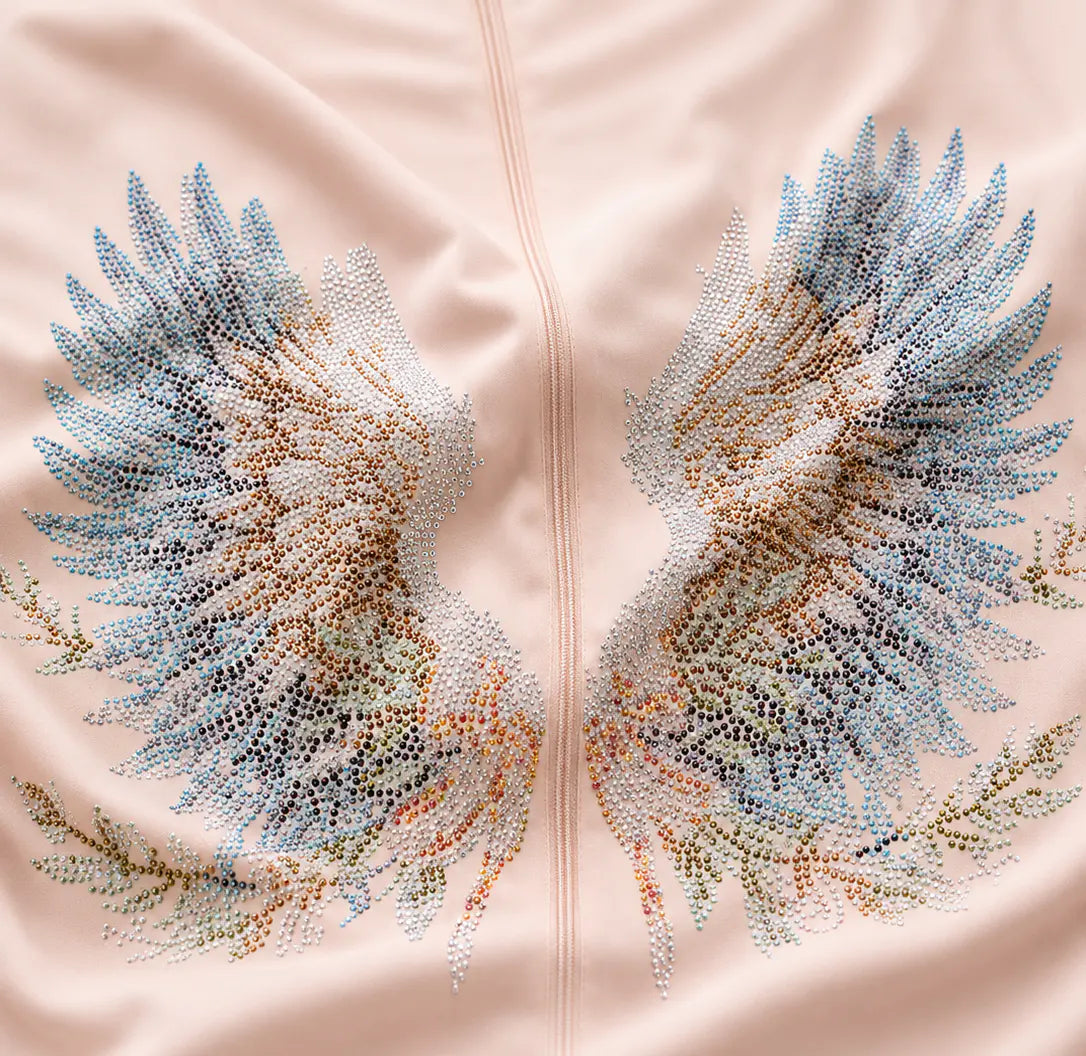 Close-up of a pale blush pink garment featuring a large embroidered wing design on each side, made from multicolored sequins and beads in shades of blue, beige, peach, and green. TCH Angel Wings Rhinestone Zip-Up Hoodie