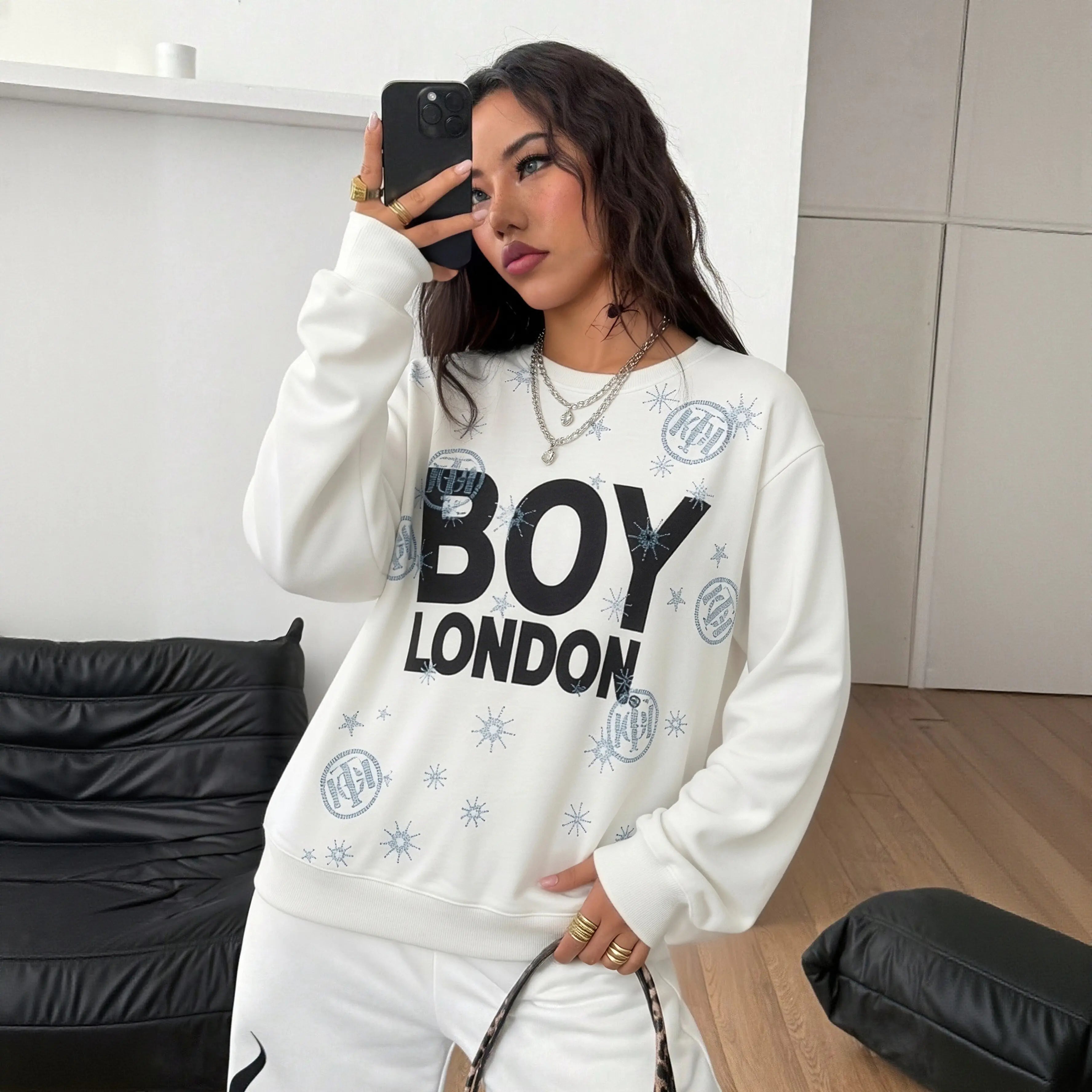 Woman wearing a 'BOY LONDON' sweatshirt taking a selfie in a room. TCH BOY LONDON Rhinestone Logo Print Crew Neck Sweatshirt
