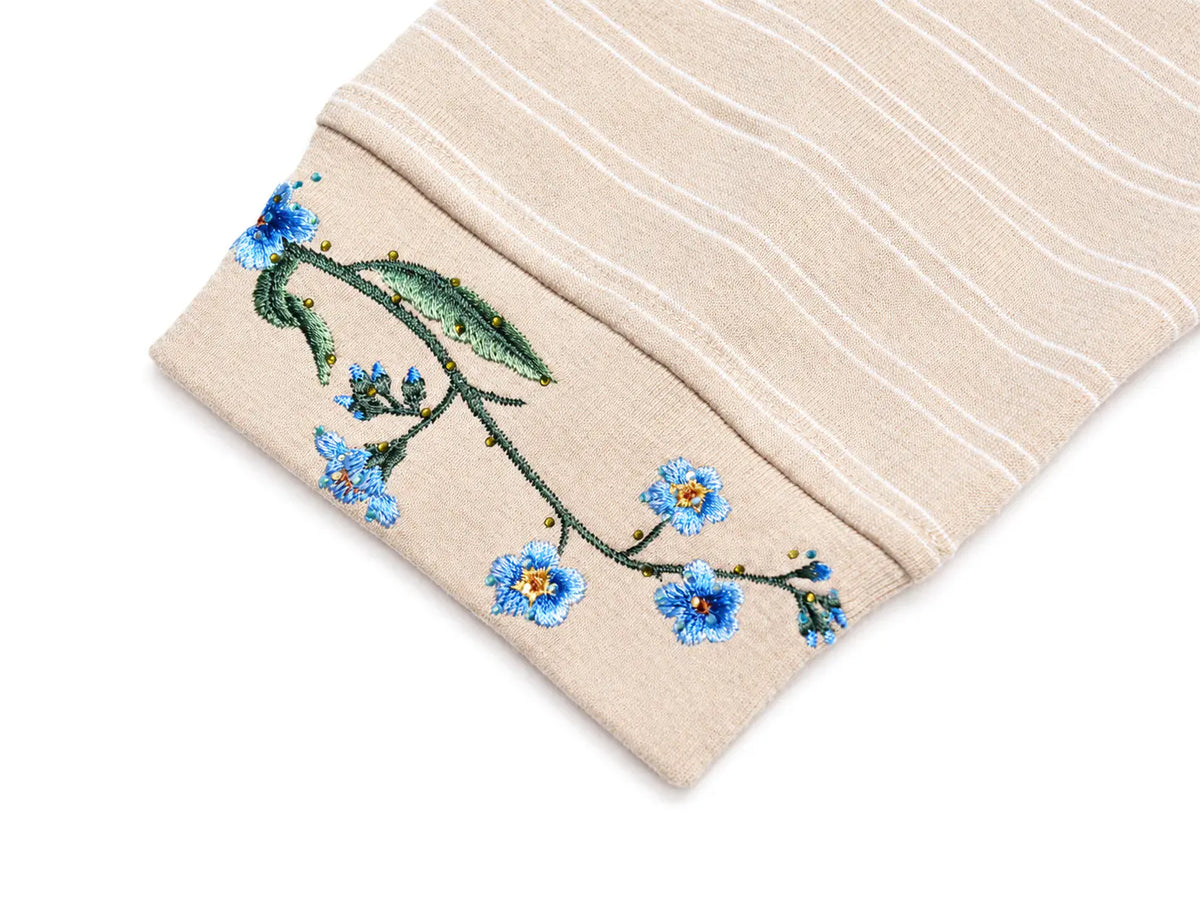 A close-up of a beige striped fabric cuff with blue and green floral embroidery featuring forget-me-nots, shown on a white background. TCH Beige Floral Embroidered Long Sleeve Polo Shirt