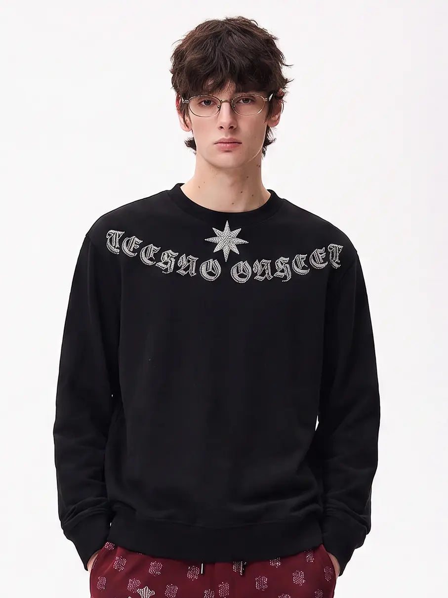 A model wearing a light blue denim jacket with various embroidered patches, including a teddy bear on the left chest and cherries on the sleeve, styled over a white t-shirt and dark pants. TCH Black Old English Techno Graphic Sweatshirt