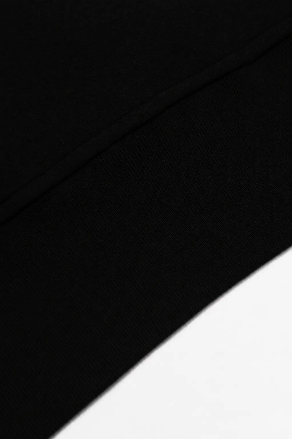 Close-up of a black fabric surface with a curved white area in the lower right corner. TCH Black Old English Techno Graphic Sweatshirt