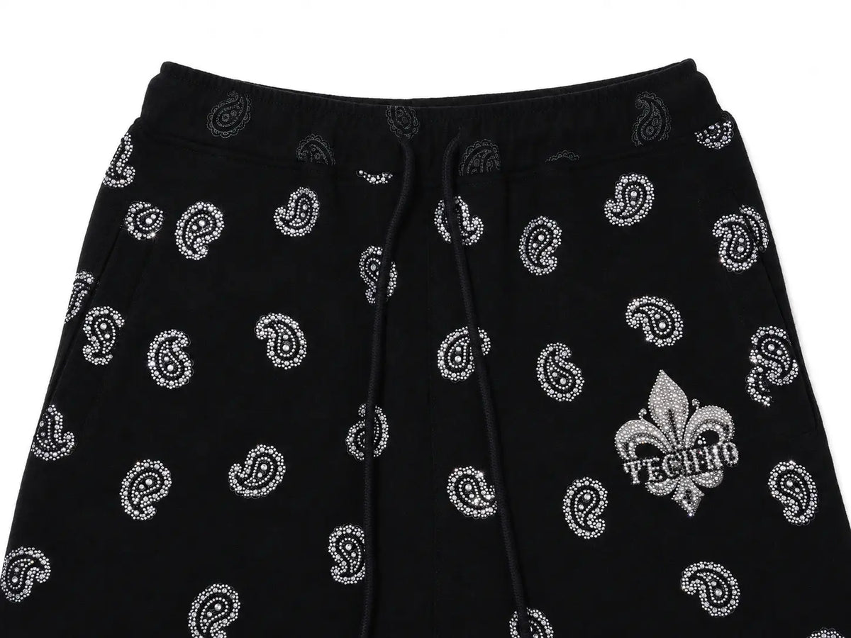 Black sweatpants with a white paisley pattern and a silver fleur-de-lis logo on the left leg, featuring a drawstring waistband. TCH Black Paisley Print Wide-Leg Sweatpants