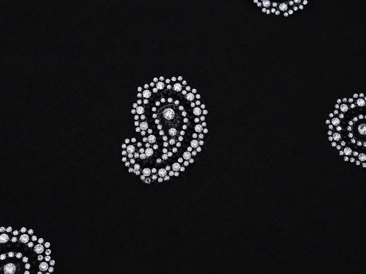 Black fabric with silver rhinestone paisley patterns, showing a close-up of the textured material. TCH Black Paisley Print Wide-Leg Sweatpants
