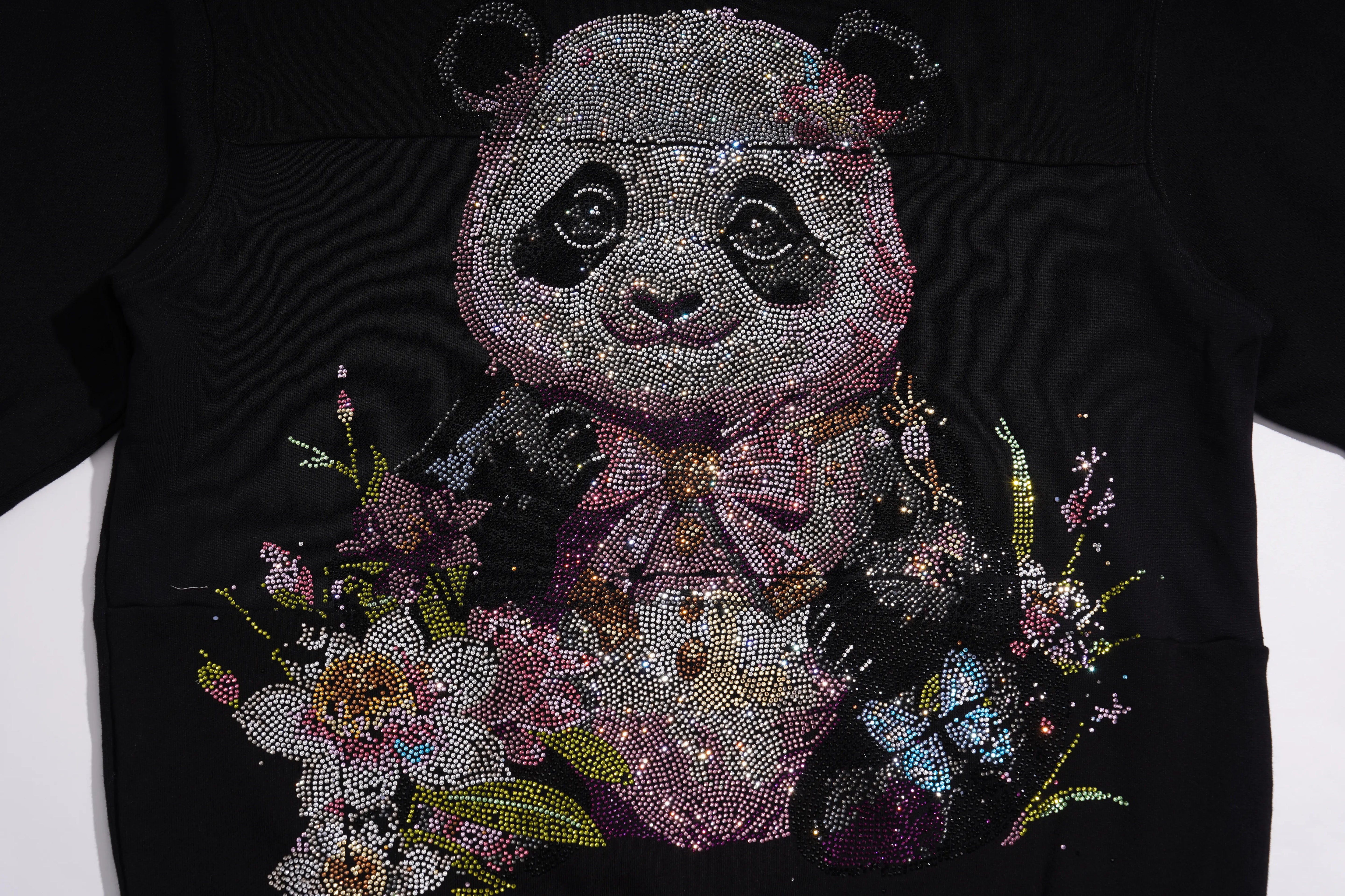 A close-up of a black garment featuring a large, highly embellished panda graphic made of rhinestones and sequins, surrounded by floral and butterfly details. TCH Black Panda Rhinestone Sweatshirt