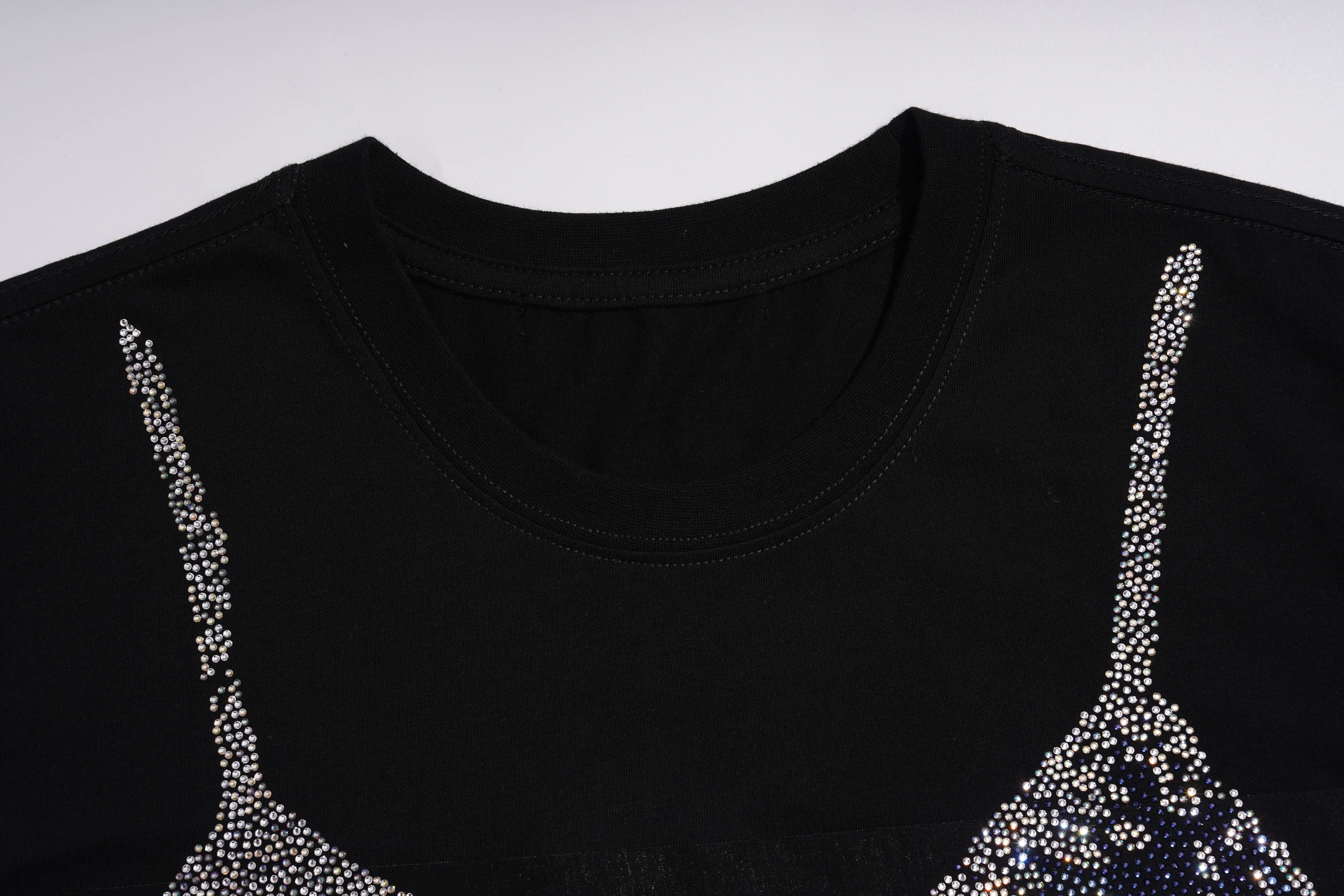 Close-up of a black crewneck t-shirt featuring rhinestone-embellished spaghetti straps resembling bra cups, set against a plain light gray background. TCH Black Rhinestone Corset Graphic T-Shirt