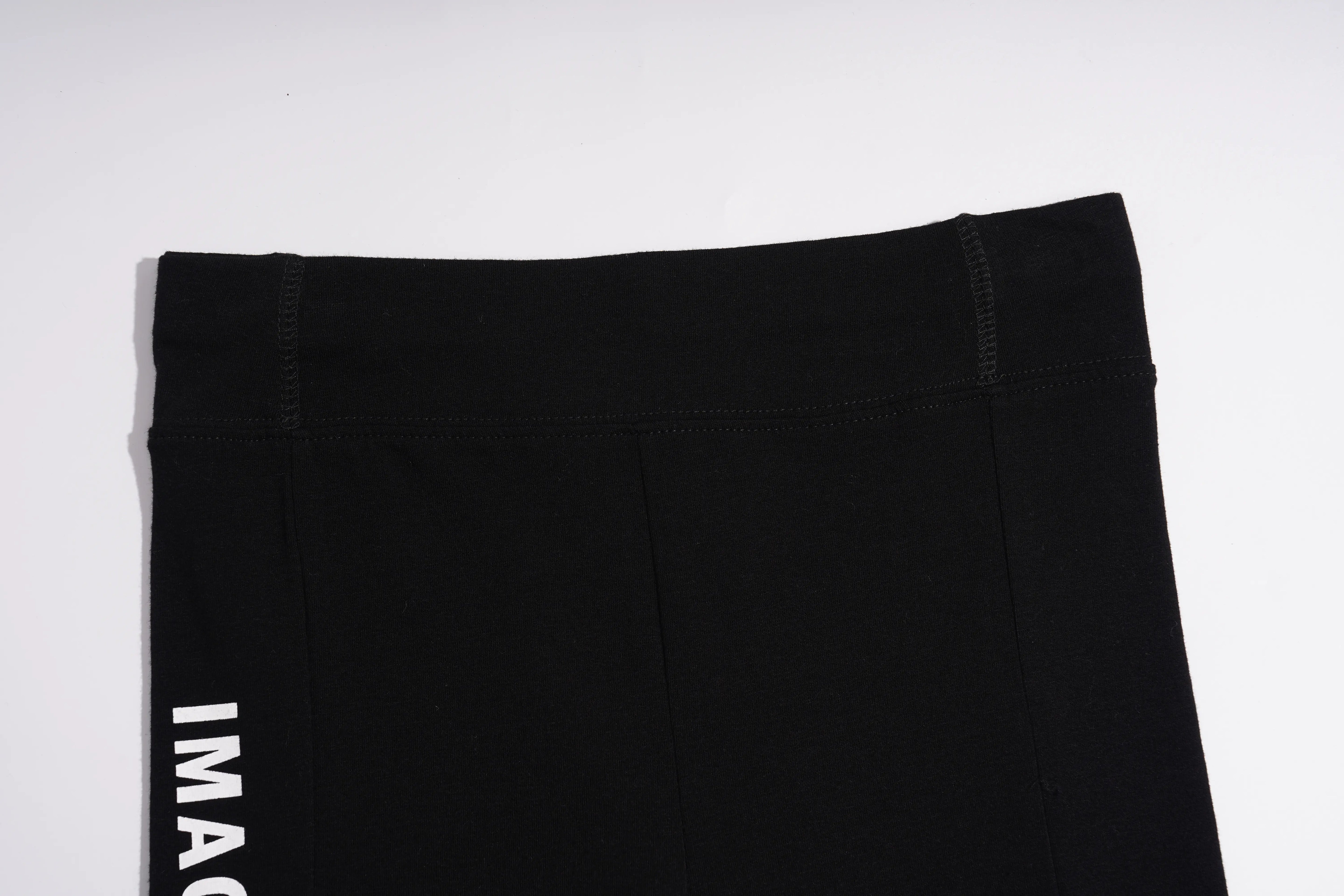 Close-up of black athletic leggings showing the waistband and a partial white vertical logo reading 'IMAG' on the left leg, photographed against a plain white background. TCH Black Rhinestone Floral Leggings