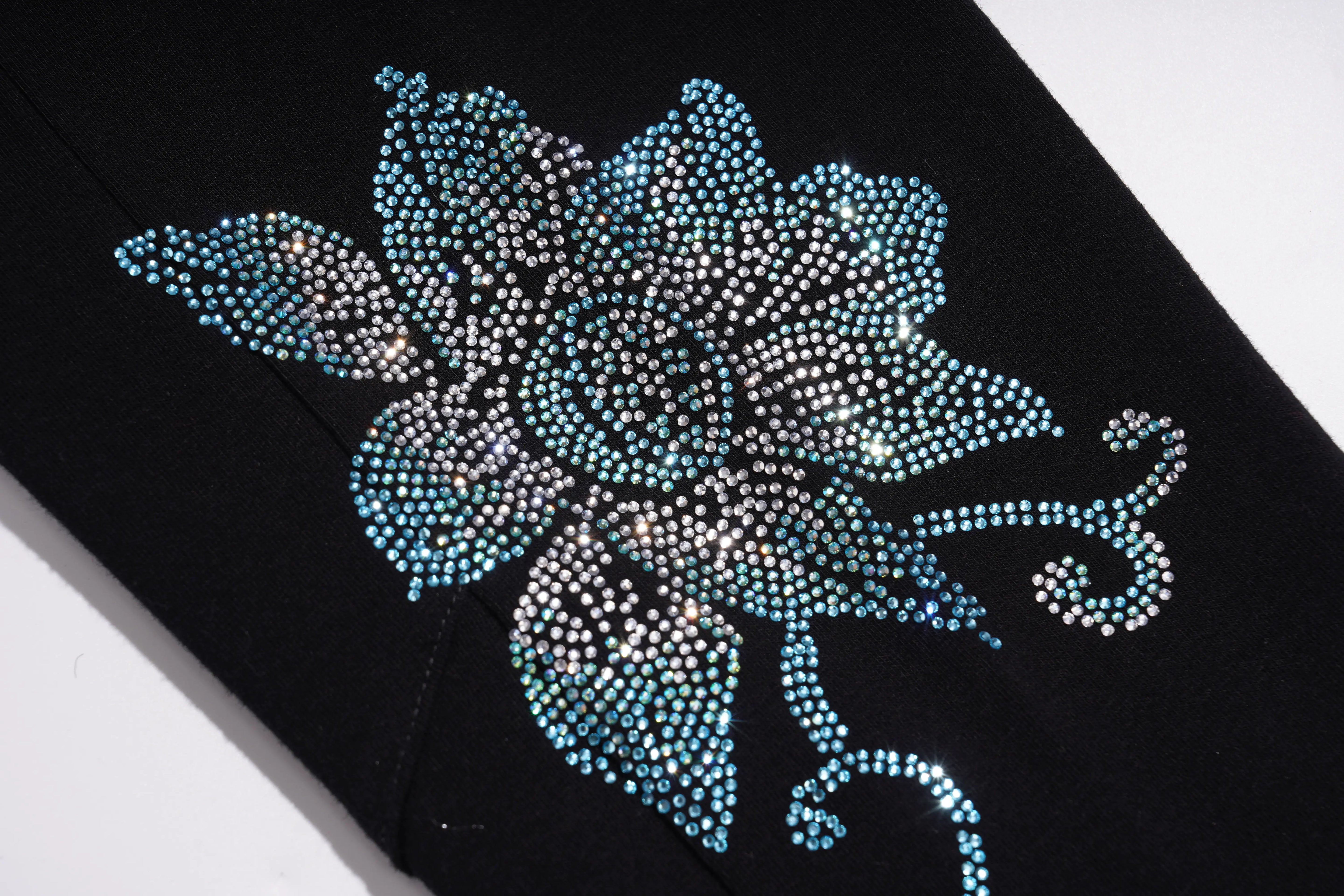 A close-up of a black garment featuring a large floral embellishment made of rhinestones in light blue, silver, and white, set against a plain white background. TCH Black Rhinestone Floral Leggings