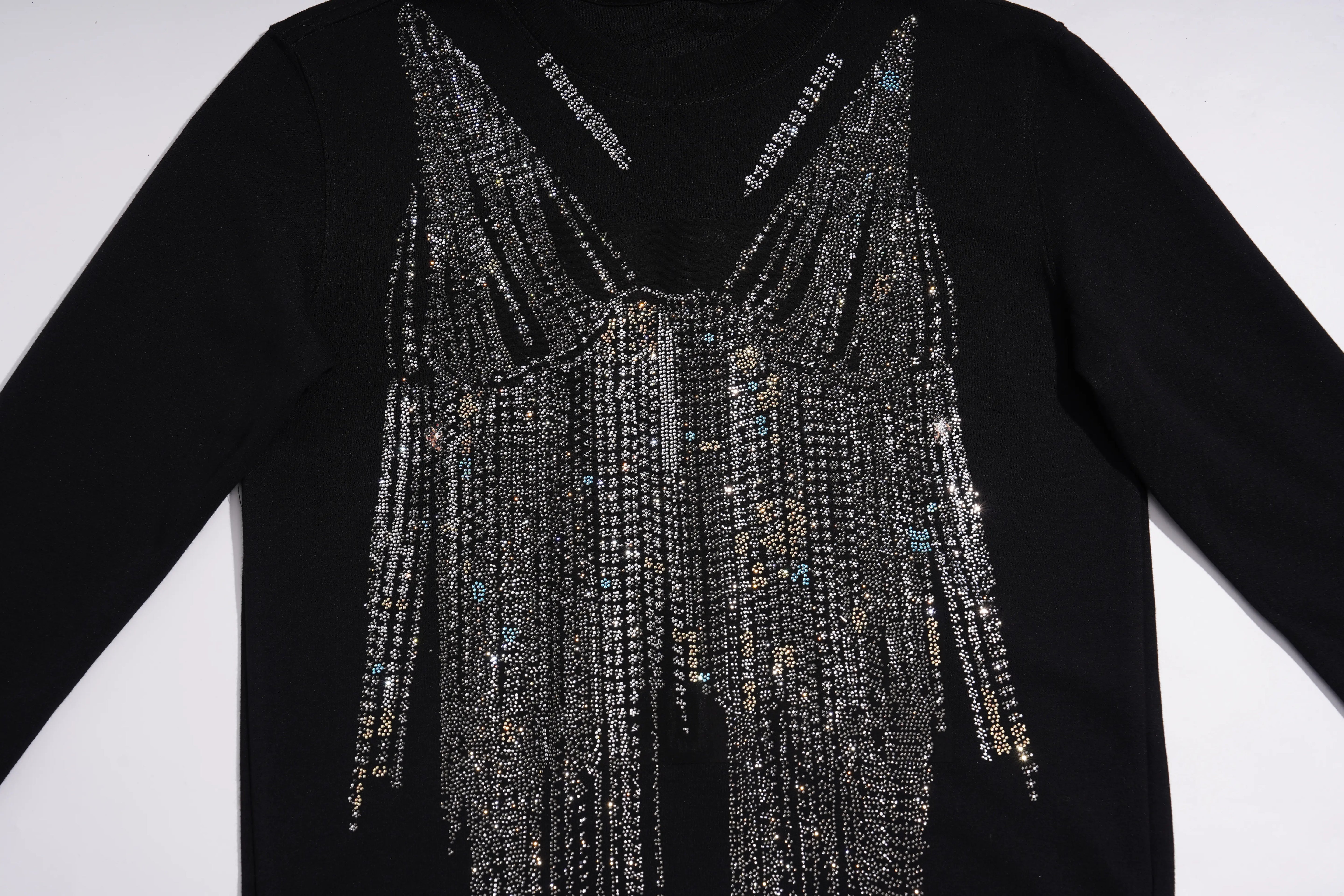 A black long-sleeve top featuring a dramatic, elaborate fringe embellishment across the V-neckline. The fringes are composed of silver rhinestones, clear crystals, and small blue bead accents, hanging in cascading strands down the front of the garment. TCH Black Rhinestone Fringe Detail Long Sleeve Mini Dress