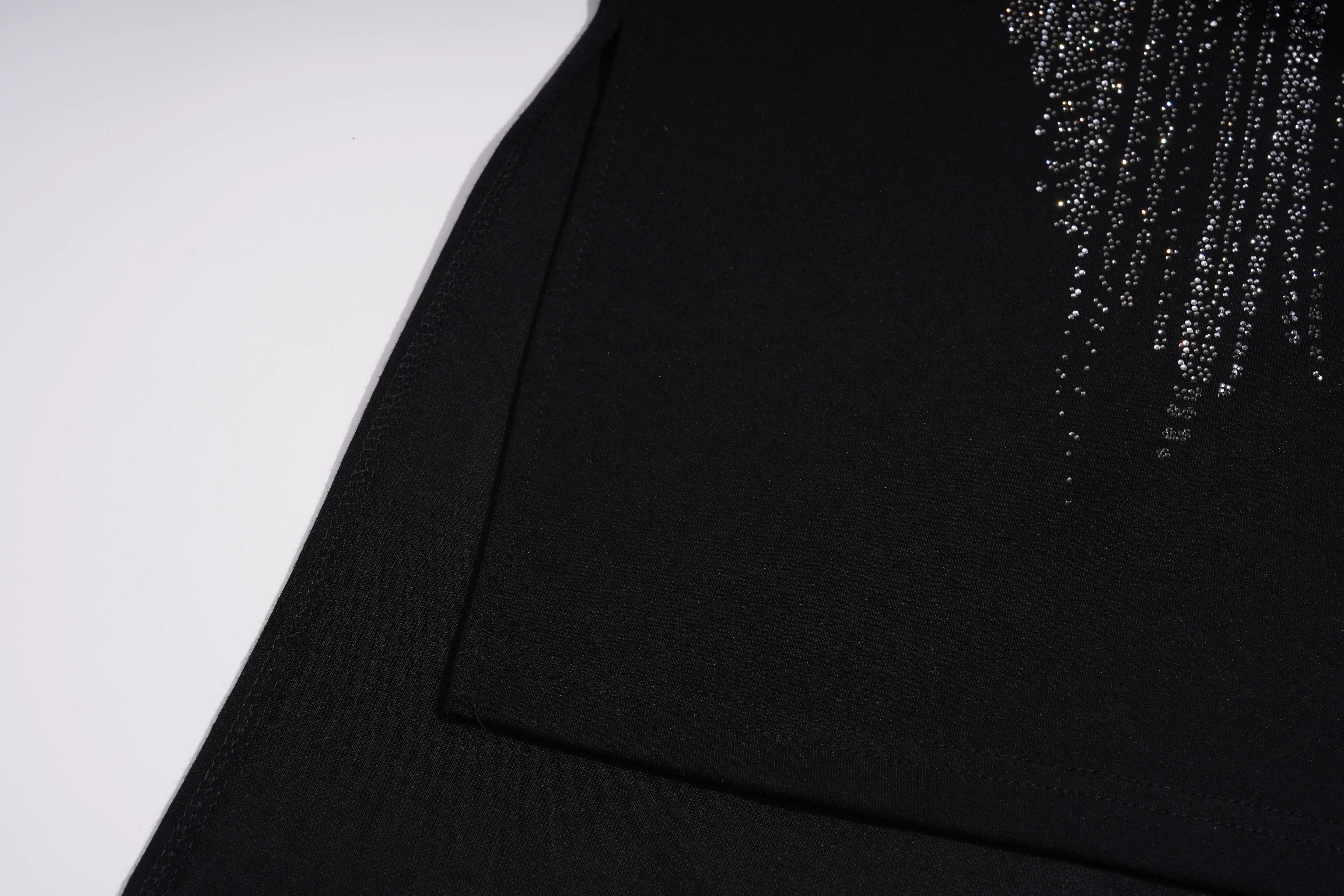 Close-up of a black garment featuring a diagonal seam and a cascading fringe embellishment made of silver rhinestones on the upper right side, set against a plain white background. TCH Black Rhinestone Fringe Detail Long Sleeve Mini Dress