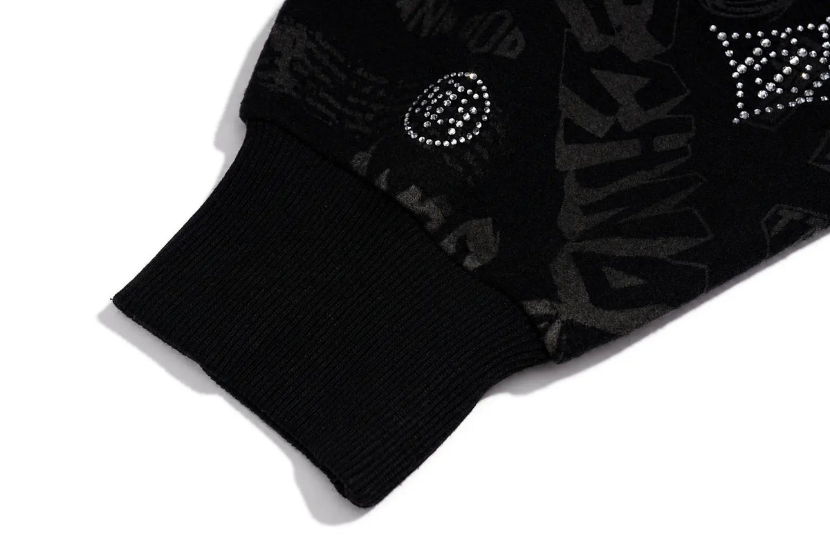 Close-up of a black ribbed knit sleeve cuff with a black-and-gray tonal graphic pattern and rhinestone embellishments on a white background. TCH Black Rhinestone Monogram Zip Up Hoodie Jacket