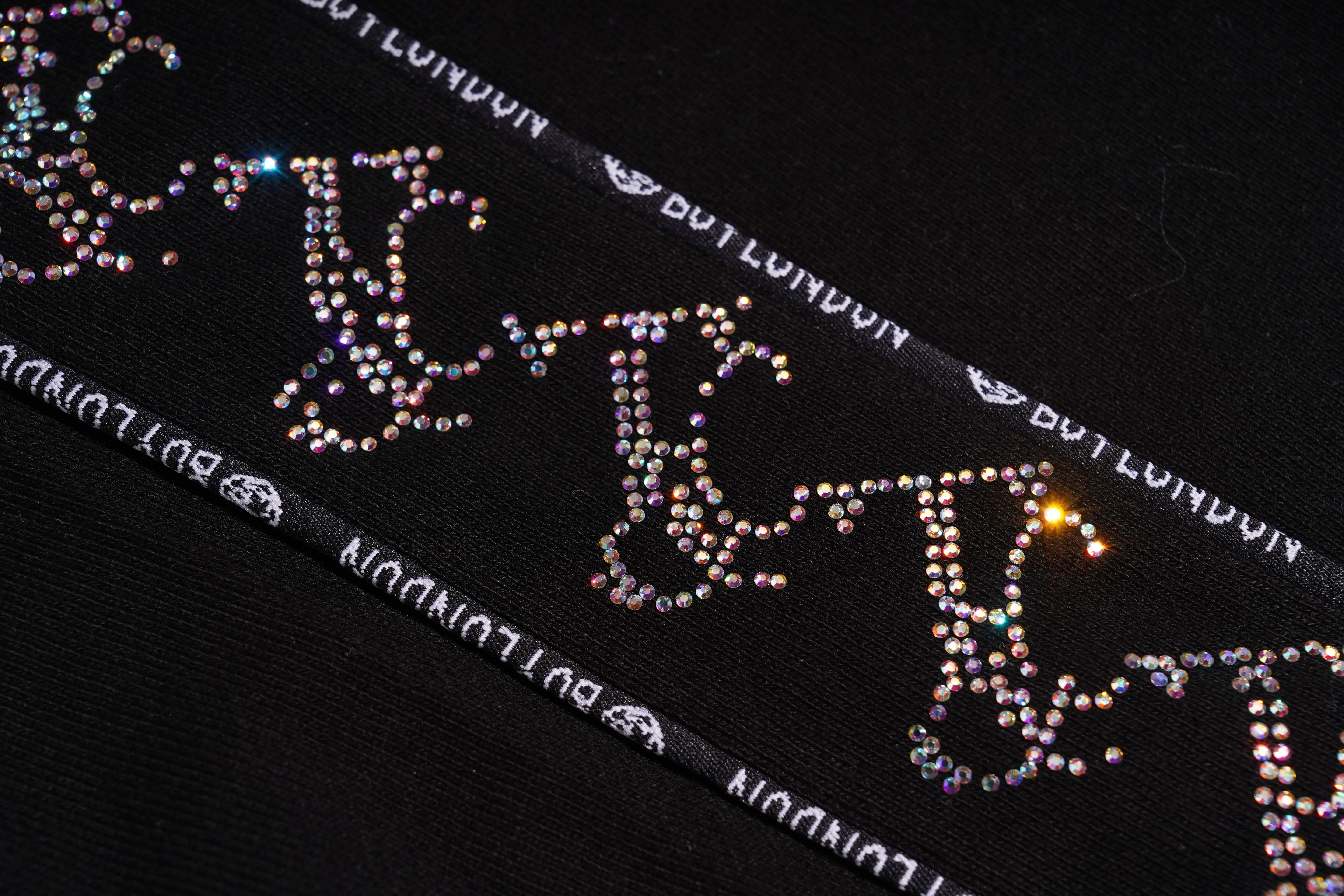 Close-up of a decorative ribbon with rhinestone letters on a black background, TCH Black Rhinestone Side Stripe Jogger Pants