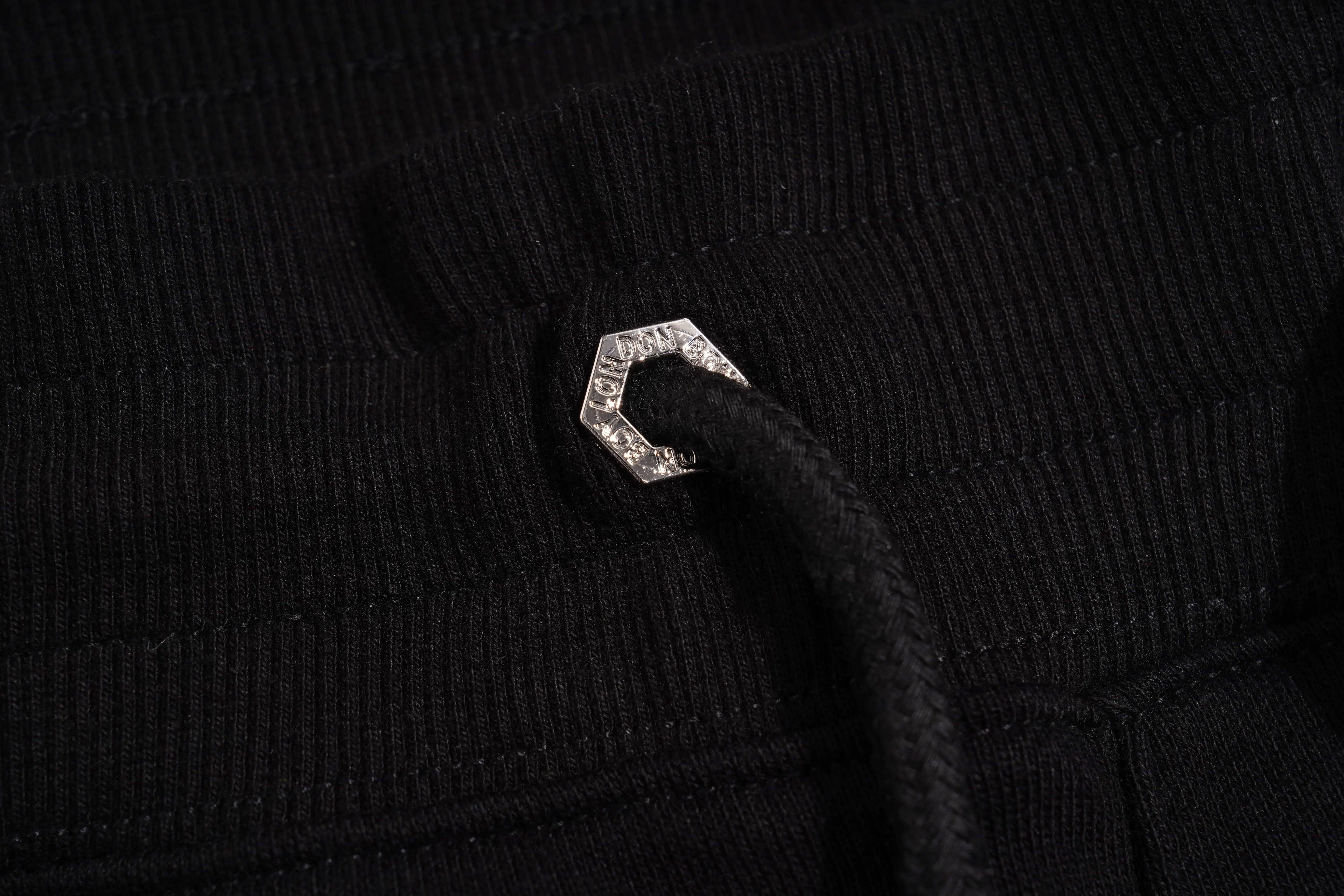 Close-up of a black textured fabric with a metallic hexagonal button. TCH Black Rhinestone Side Stripe Jogger Pants