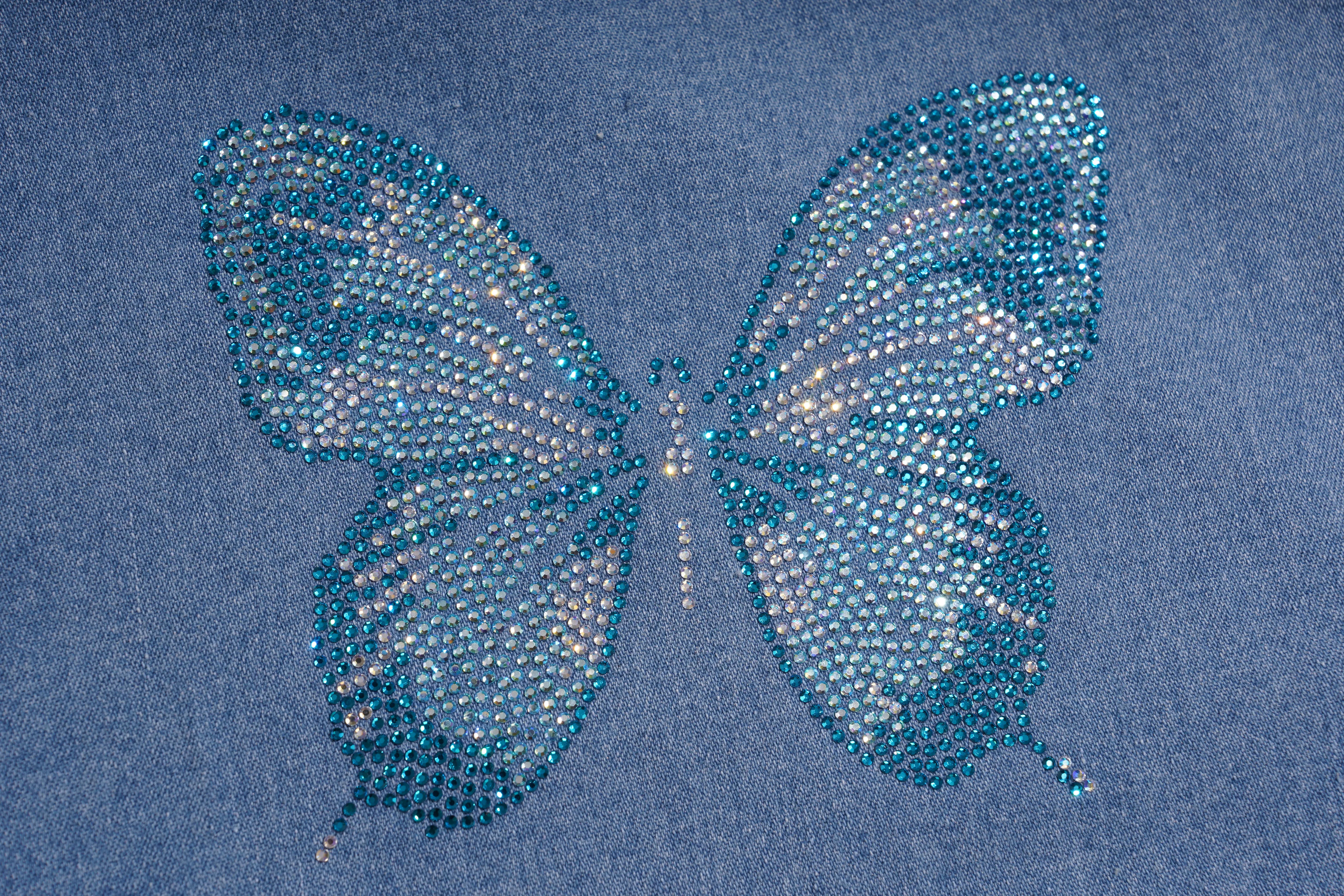 A butterfly-shaped embellishment made of blue rhinestones on a blue denim fabric background. TCH Blue Butterfly & Teddy Bear Lace Hem Denim Jeans