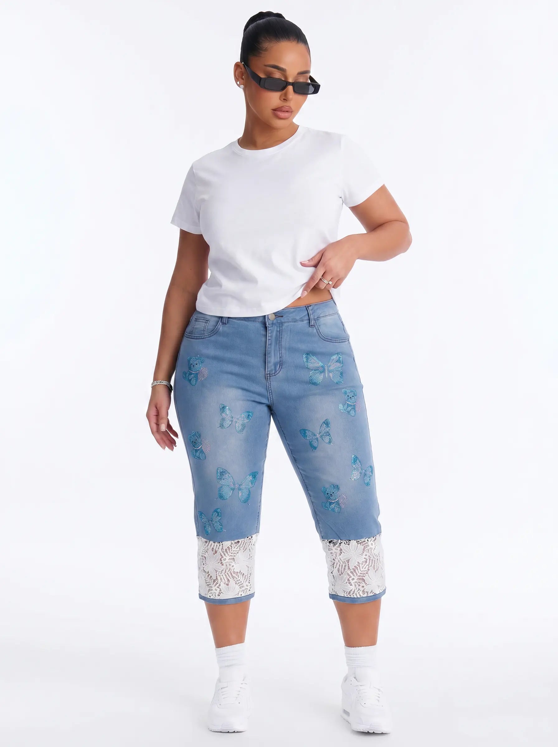 A model wearing light blue cropped denim jeans with blue butterfly prints and white lace trim at the hem, styled with a white t-shirt, white sneakers, and sunglasses against a white studio background. TCH Blue Butterfly & Teddy Bear Lace Hem Denim Jeans