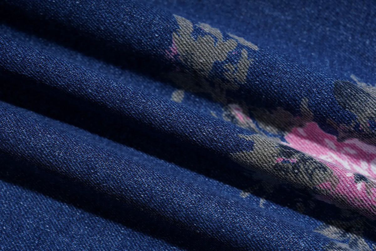 A close-up of dark blue fabric with a subtle floral pattern in pink, beige, and gray, draped in soft folds. TCH Blue Floral Butterfly Rhinestone Wide-Leg Jeans