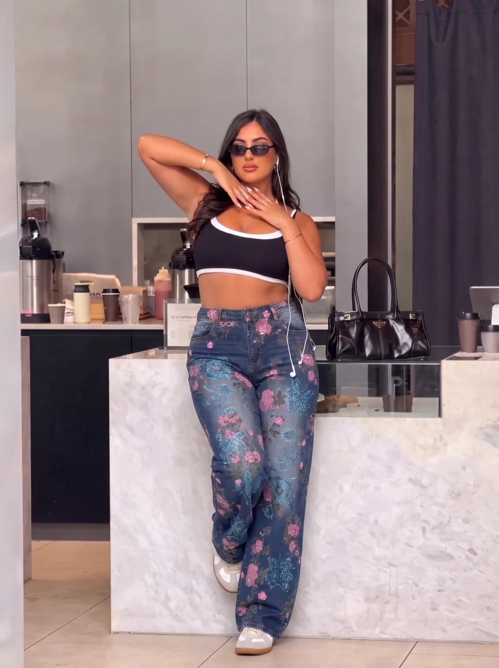 A woman posing in a modern kitchen setting, wearing a black and white crop top, blue floral wide-leg jeans, and white sneakers. TCH Blue Floral Butterfly Rhinestone Wide-Leg Jeans
