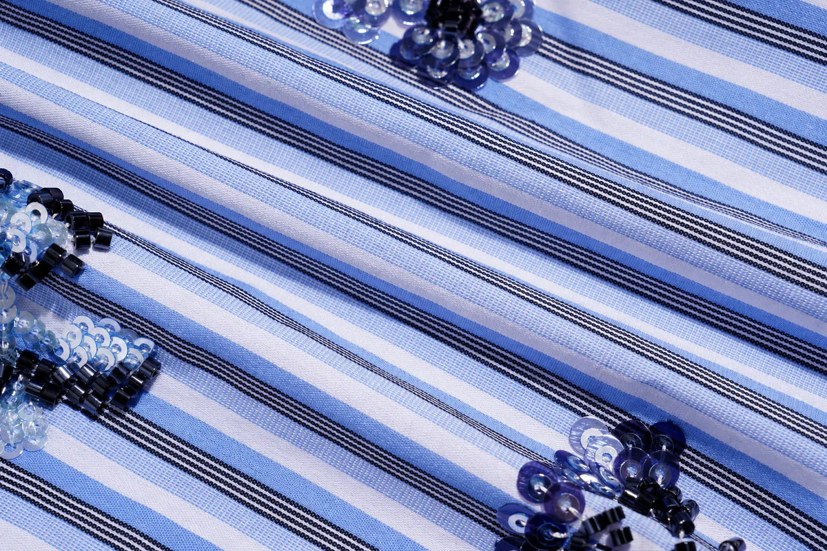 A close-up of a blue and white striped fabric with decorative sequin embellishments in shades of blue, black, and white. TCH Blue Floral Embroidered Pinstripe Shirt