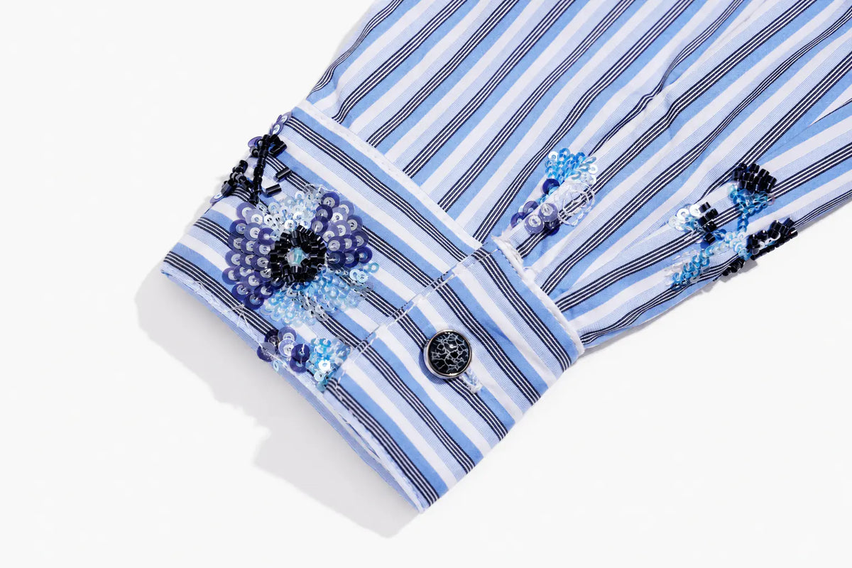 Close-up of a striped shirt cuff with blue and white vertical stripes, decorated with embroidered floral details in blue, purple, and black, and a single dark button. TCH Blue Floral Embroidered Pinstripe Shirt