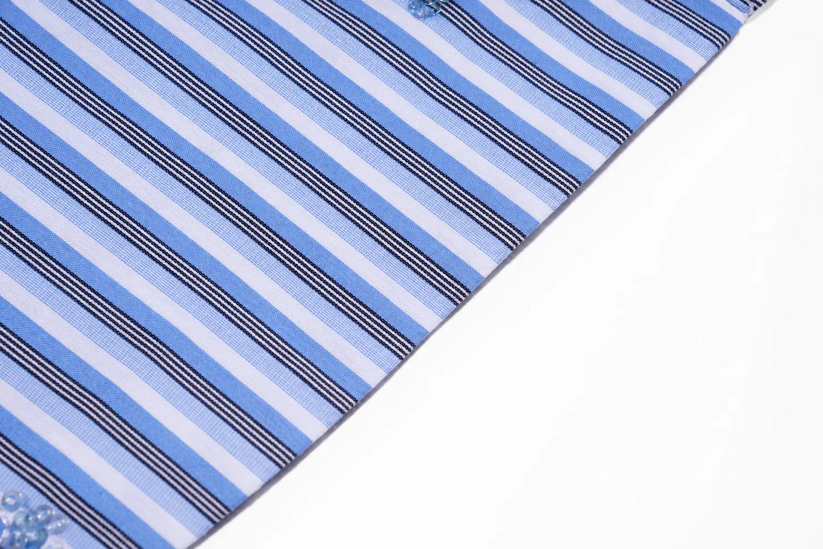 A close-up of a striped fabric, likely a bandana or pocket square, featuring diagonal stripes of light blue, navy, and white. The fabric is shown folded diagonally over a plain white background. TCH Blue Floral Embroidered Pinstripe Shirt