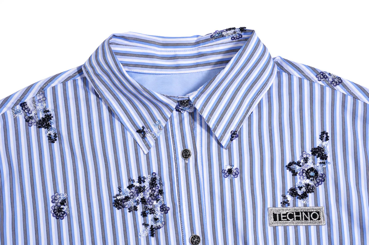 A close-up of a Techno brand button-down shirt featuring blue and white vertical stripes, embellished with dark floral embroidery and sequins on the chest and shoulders, set against a plain white background. TCH Blue Floral Embroidered Pinstripe Shirt