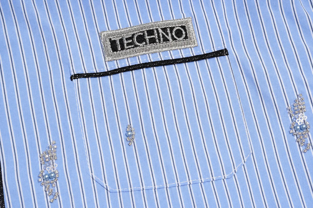 Close-up of a light blue and white pinstriped shirt pocket with a rectangular embroidered 'TECHNO' brand patch, a black decorative trim line, and small silver and blue floral embroidery. TCH Blue Pinstripe Embroidered Pocket Shirt