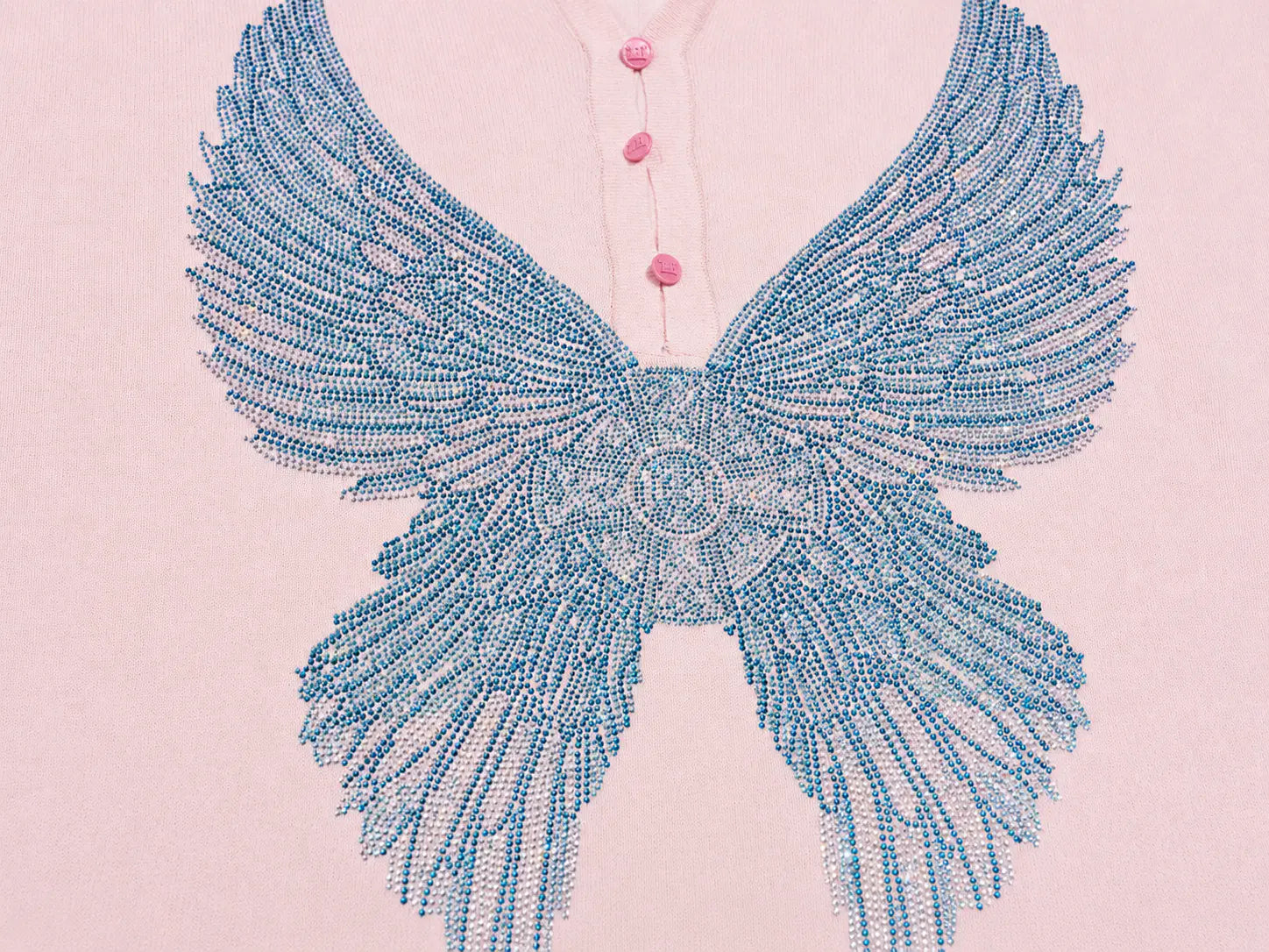 A close-up of a light pink button-front garment featuring a large blue beaded wing motif across the chest. TCH Blue Rhinestone Angel Wings Cropped Hoodie