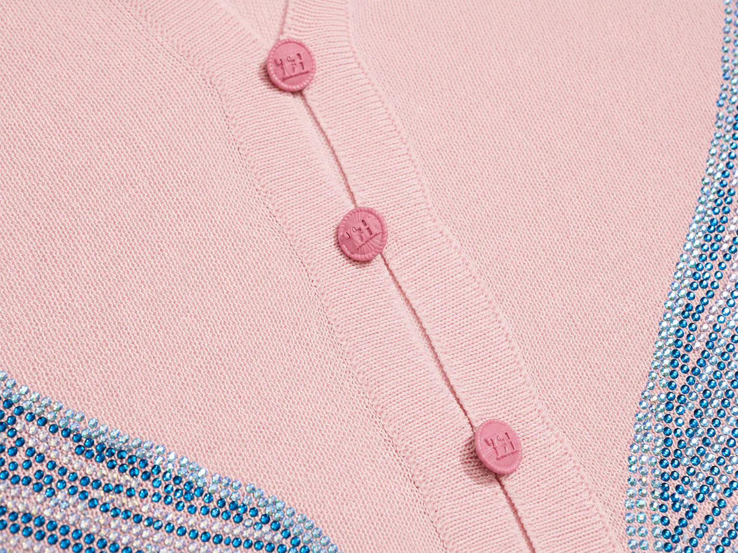 Close-up of a light pink knit cardigan with pink buttons and blue rhinestone trim along the edges. TCH Blue Rhinestone Angel Wings Cropped Hoodie