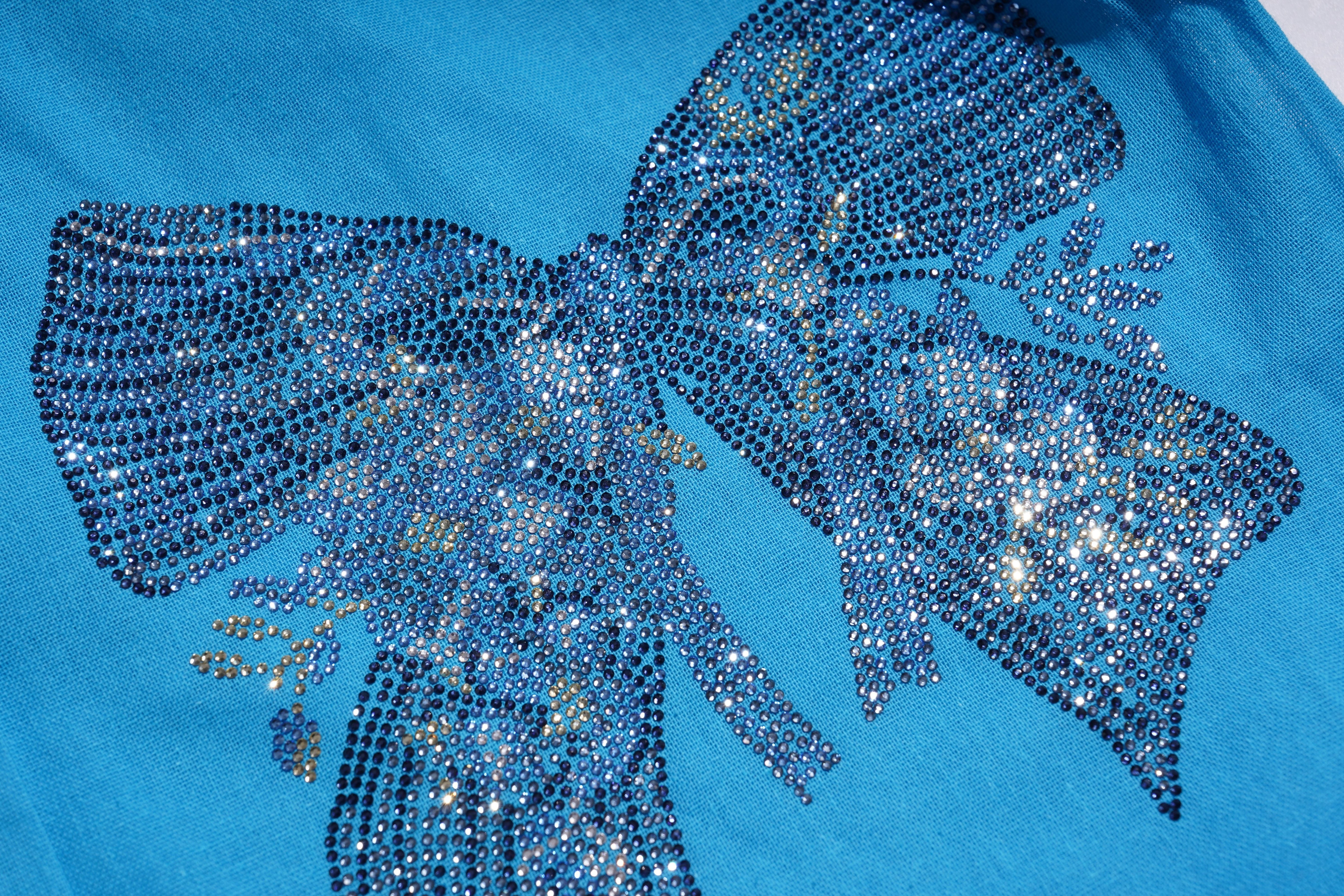 Close-up of a blue shirt with a large, decorative bow made of sequins on a blue background. TCH Blue Rhinestone Bow Matching Set