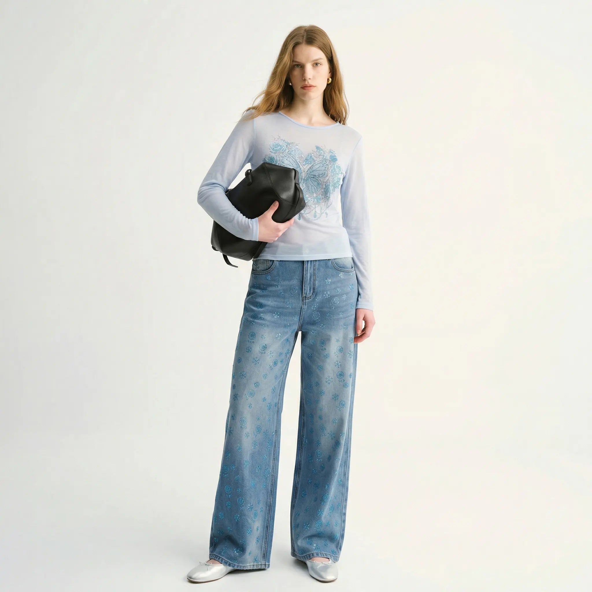Woman wearing a light blue sweater and jeans holding a black clutch against a white background, TCH Blue Snowflake Rhinestone Denim Jeans