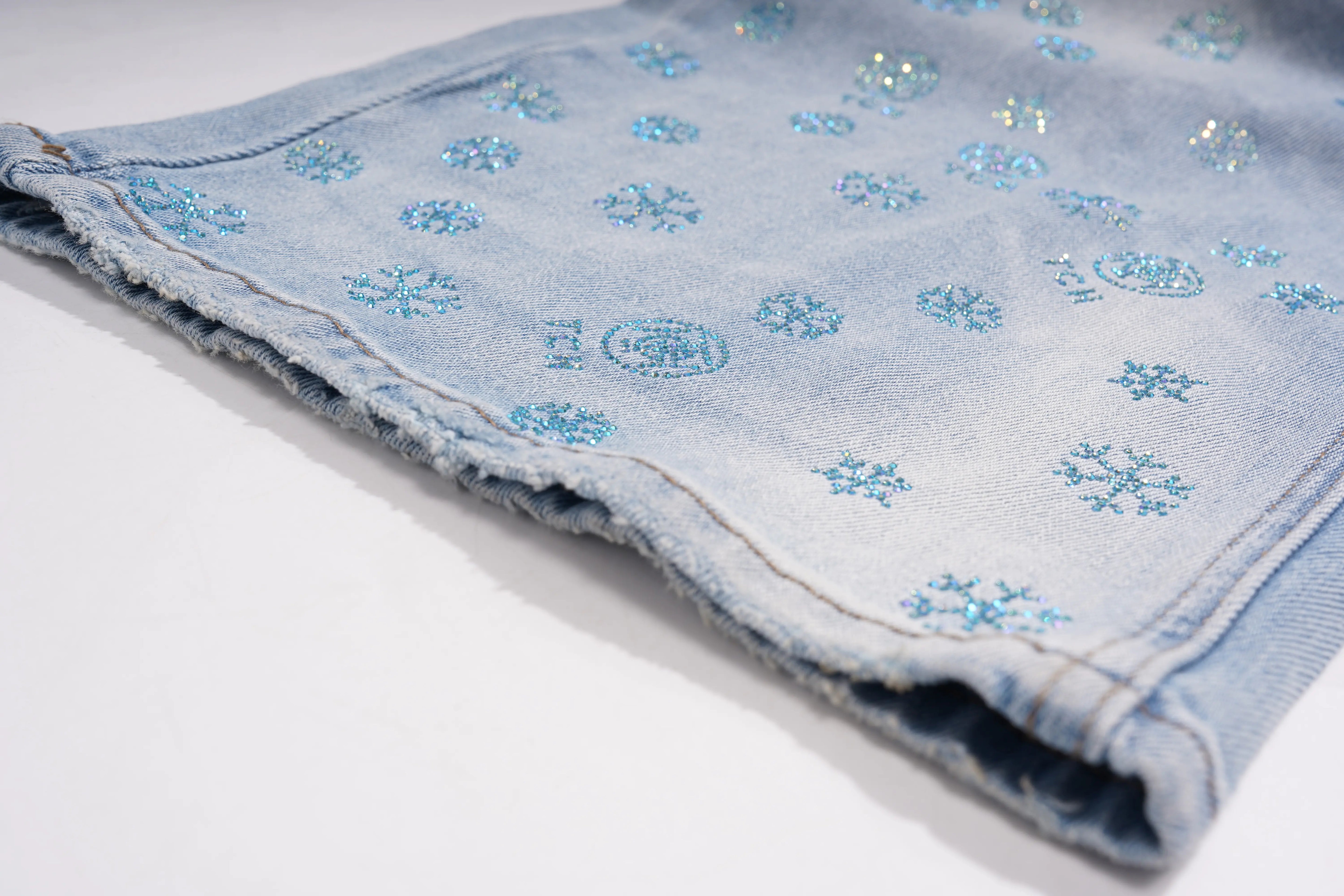 Close-up of a denim fabric with floral patterns on a white background, TCH Blue Snowflake Rhinestone Denim Jeans