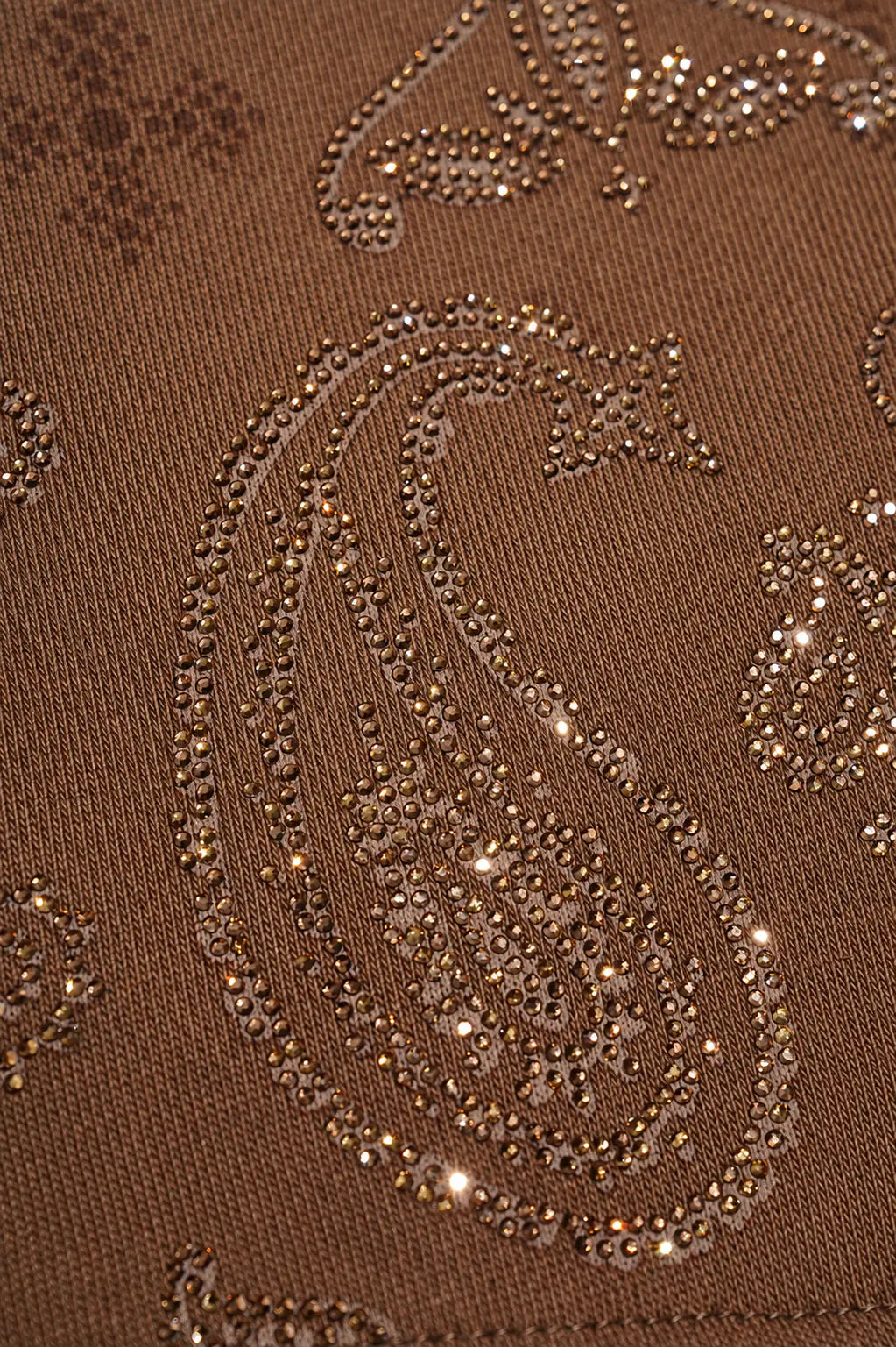 Close-up of a brown knit fabric featuring a paisley pattern embellished with shimmering sequins and rhinestones. TCH Brown Rhinestone Paisley Zip Up Hoodie