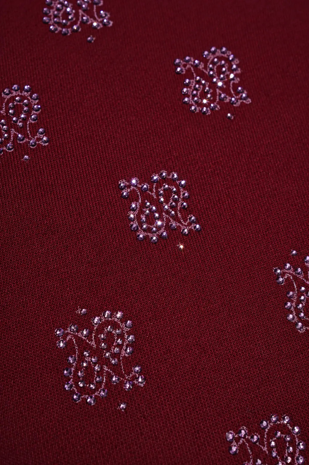 A close-up of a deep maroon fabric with repeating silver paisley motifs embellished with small rhinestones. TCH Burgundy Paisley Print Wide-Leg Sweatpants with Cross Graphic