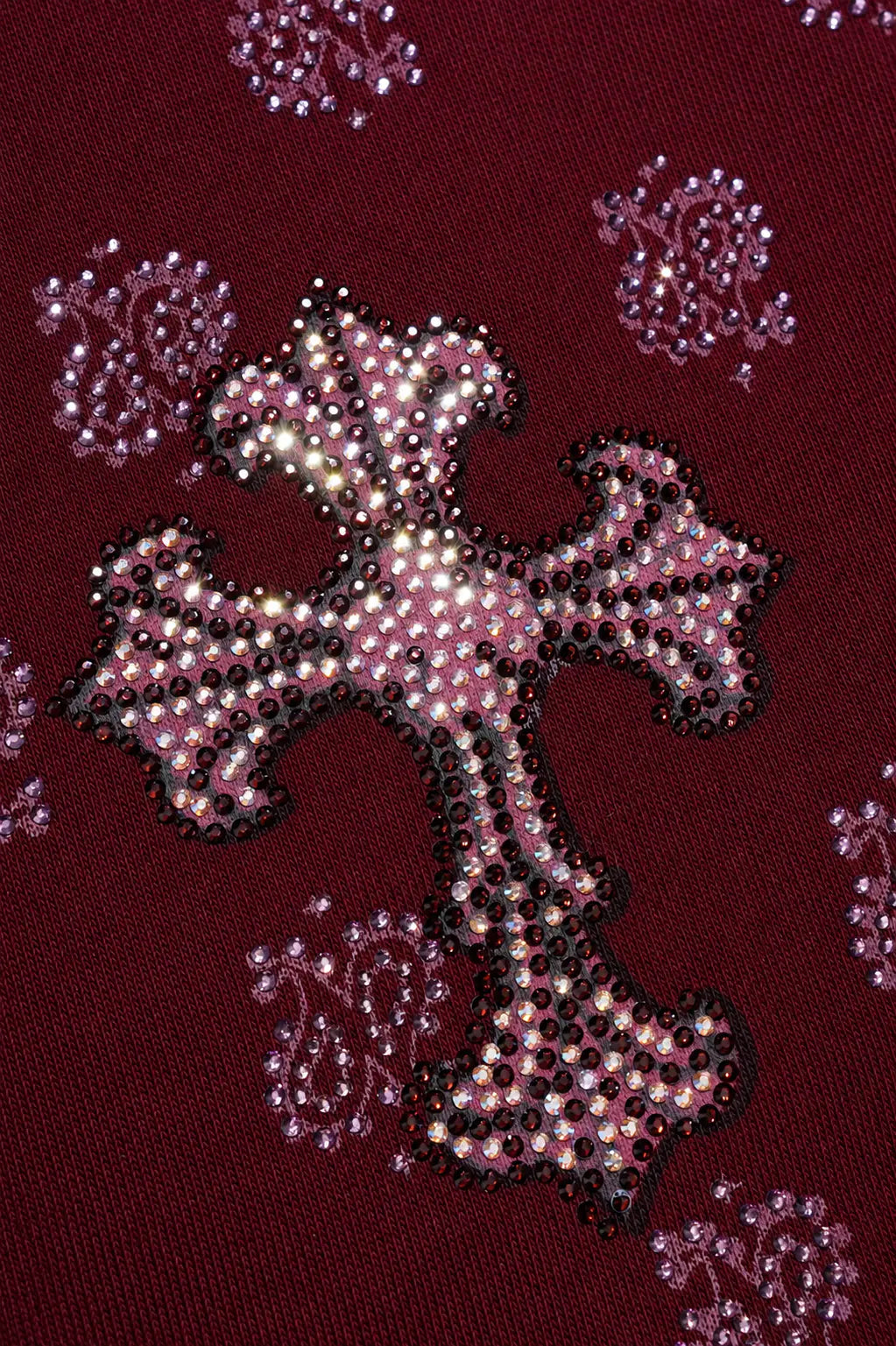 A close-up of a burgundy knit fabric featuring a large central cross embellished with pink rhinestones and black beaded outlines, surrounded by smaller matching pink and black rhinestone motifs. TCH Burgundy Paisley Print Wide-Leg Sweatpants with Cross Graphic
