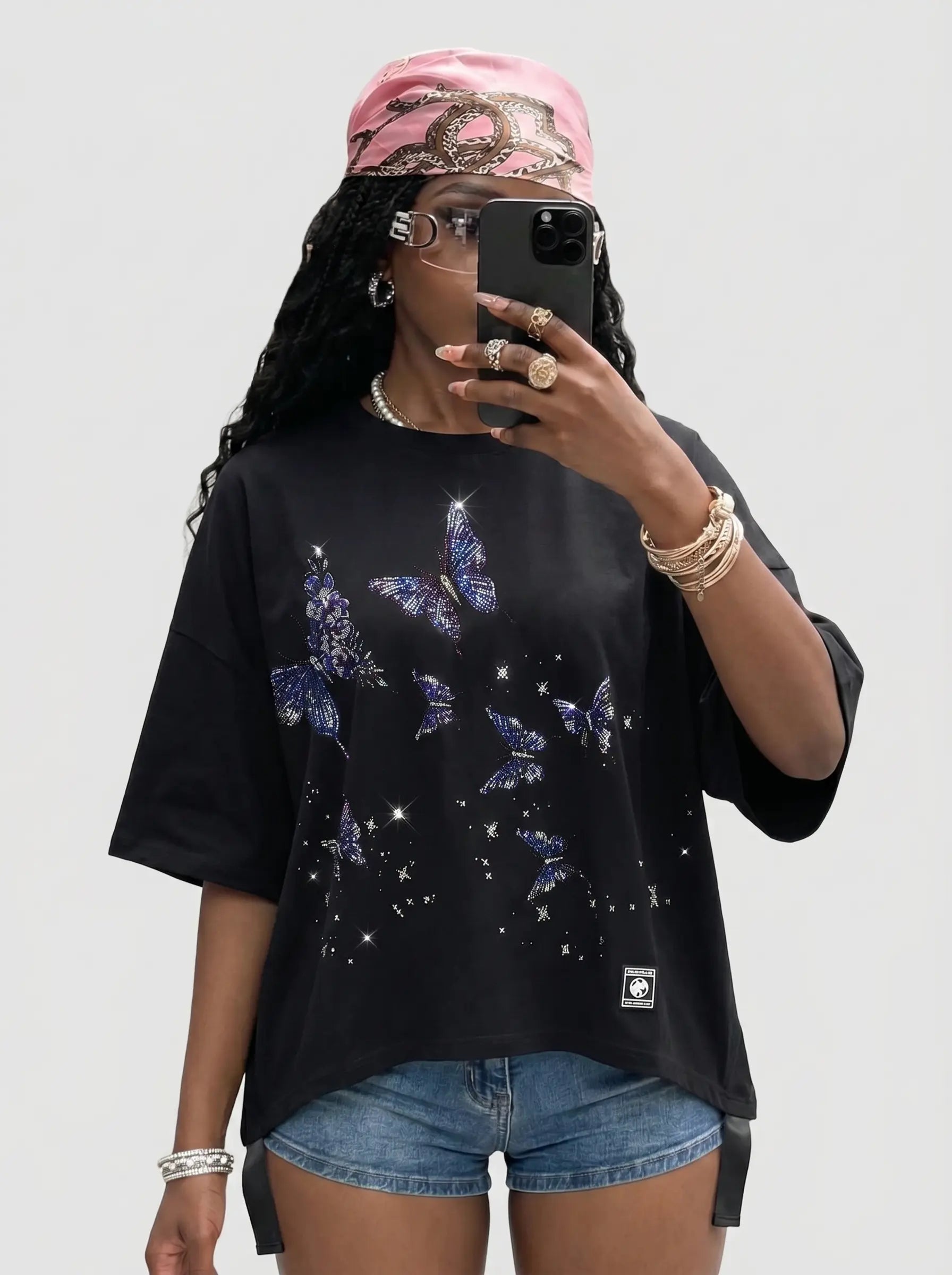 Person wearing a black t-shirt with butterfly designs and denim shorts, taking a mirror selfie. TCH Butterfly Rhinestone Oversized T-Shirt