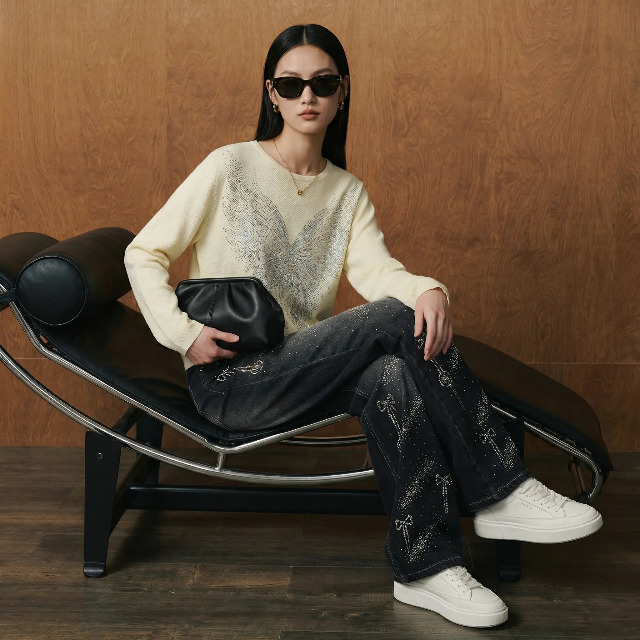 Woman sitting on a modern black chair holding a black clutch against a wooden background, TCH Celestial Rhinestone Wide-Leg Black Jeans