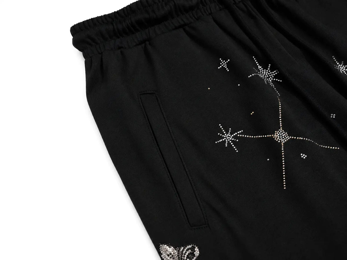 Close-up of black drawstring pants with silver rhinestone star and butterfly embellishments, shown on a white background. TCH Celestial Rhinestone Wide-Leg Sweatpants