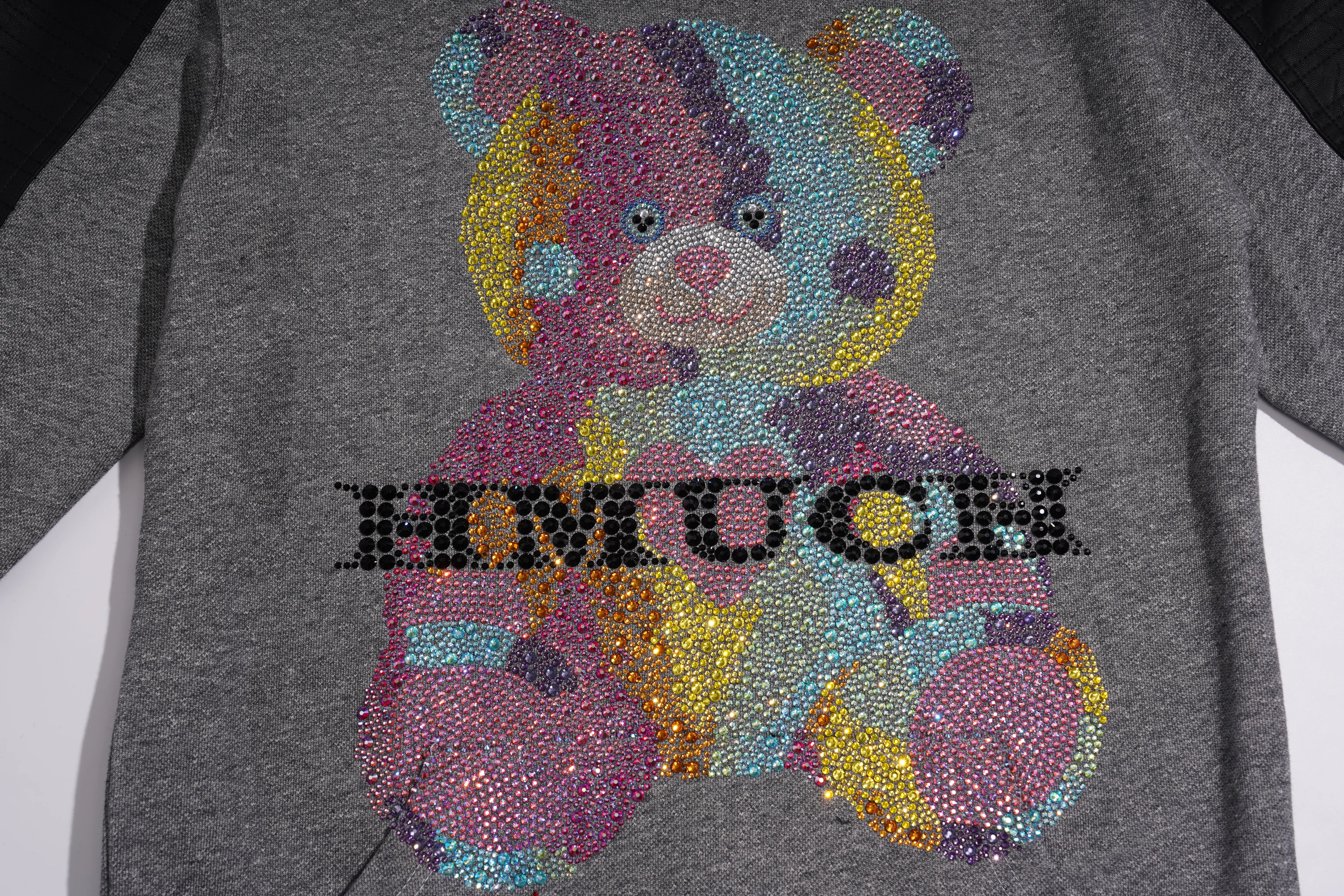A close-up of a heather gray long-sleeve top featuring a large teddy bear graphic made of colorful rhinestones and the word 'EMUCH' across the front. TCH Colorful Rhinestone Teddy Bear Crewneck Sweatshirt